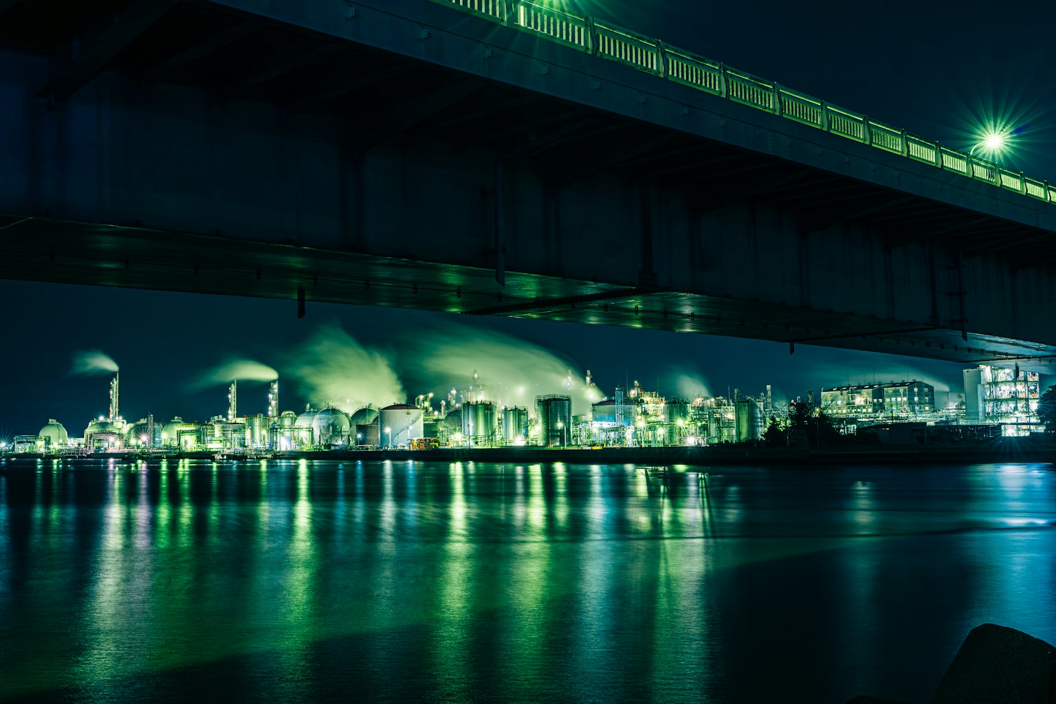 Night view of an industrial area under a bridge Factory lights reflecting on the water