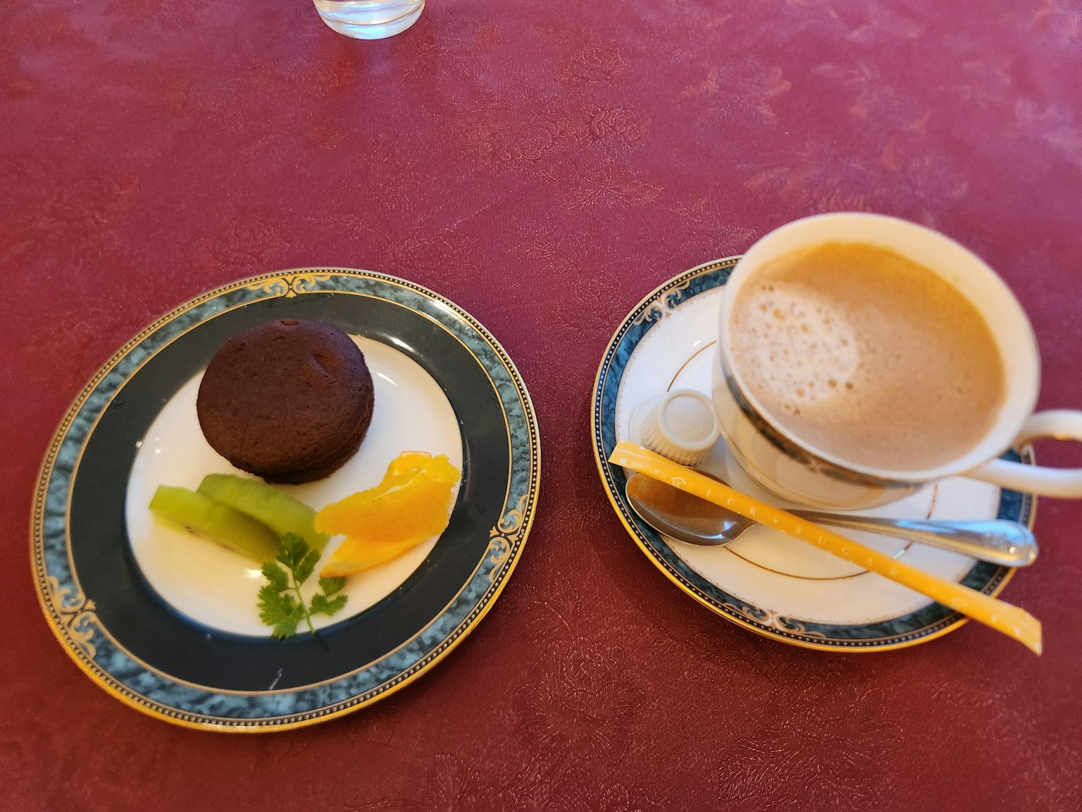 Ein Teller mit Schokoladendessert und Obst neben einer Tasse Kaffee auf einem roten Tischdecken