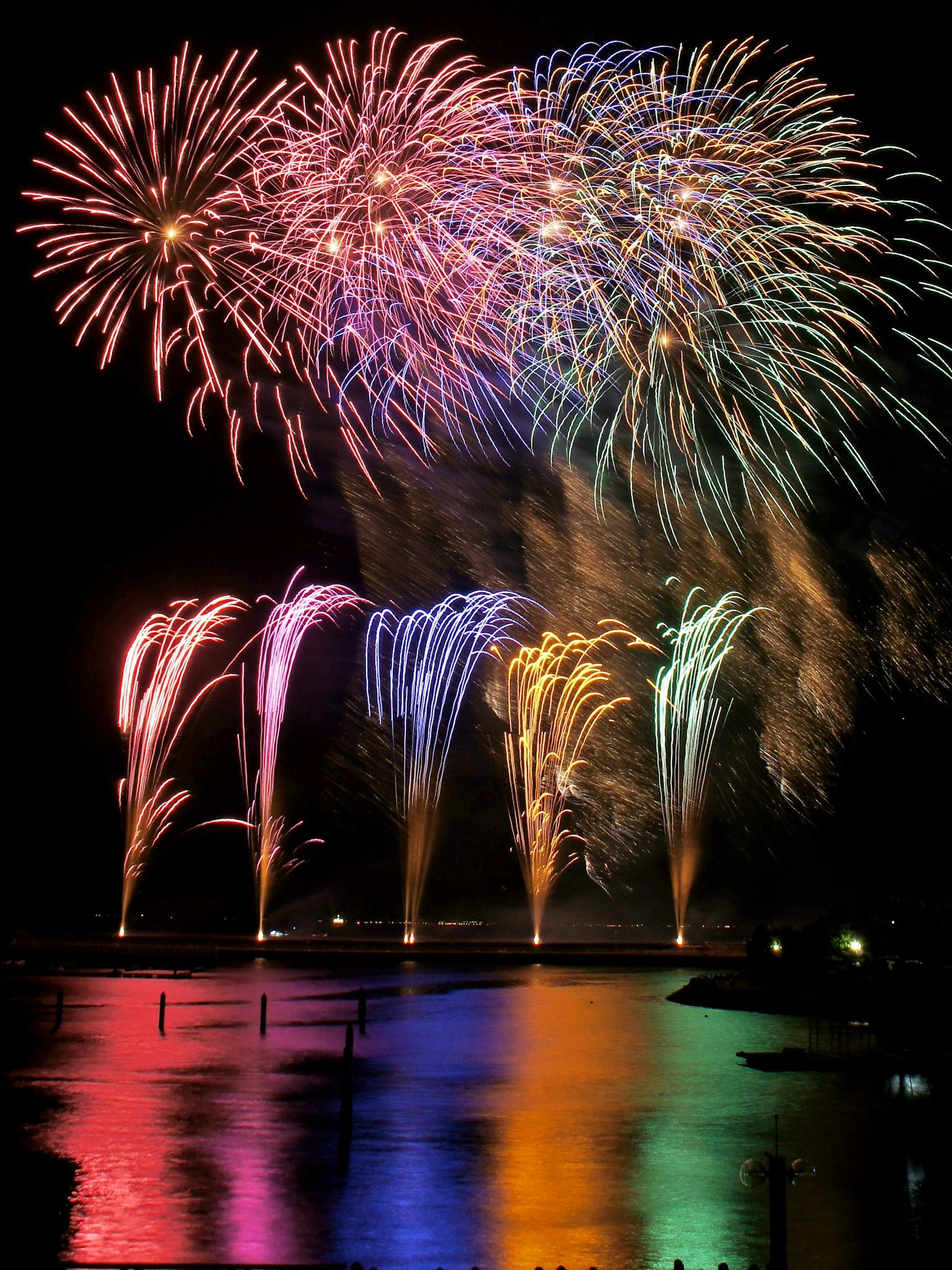Des feux d'artifice colorés explosent dans le ciel nocturne se reflétant sur l'eau