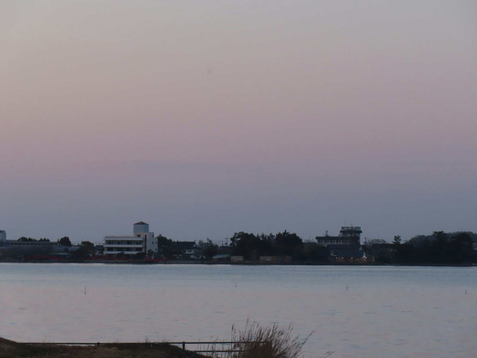 Vista serena del lago con un cielo crepuscolare soffuso e edifici in lontananza