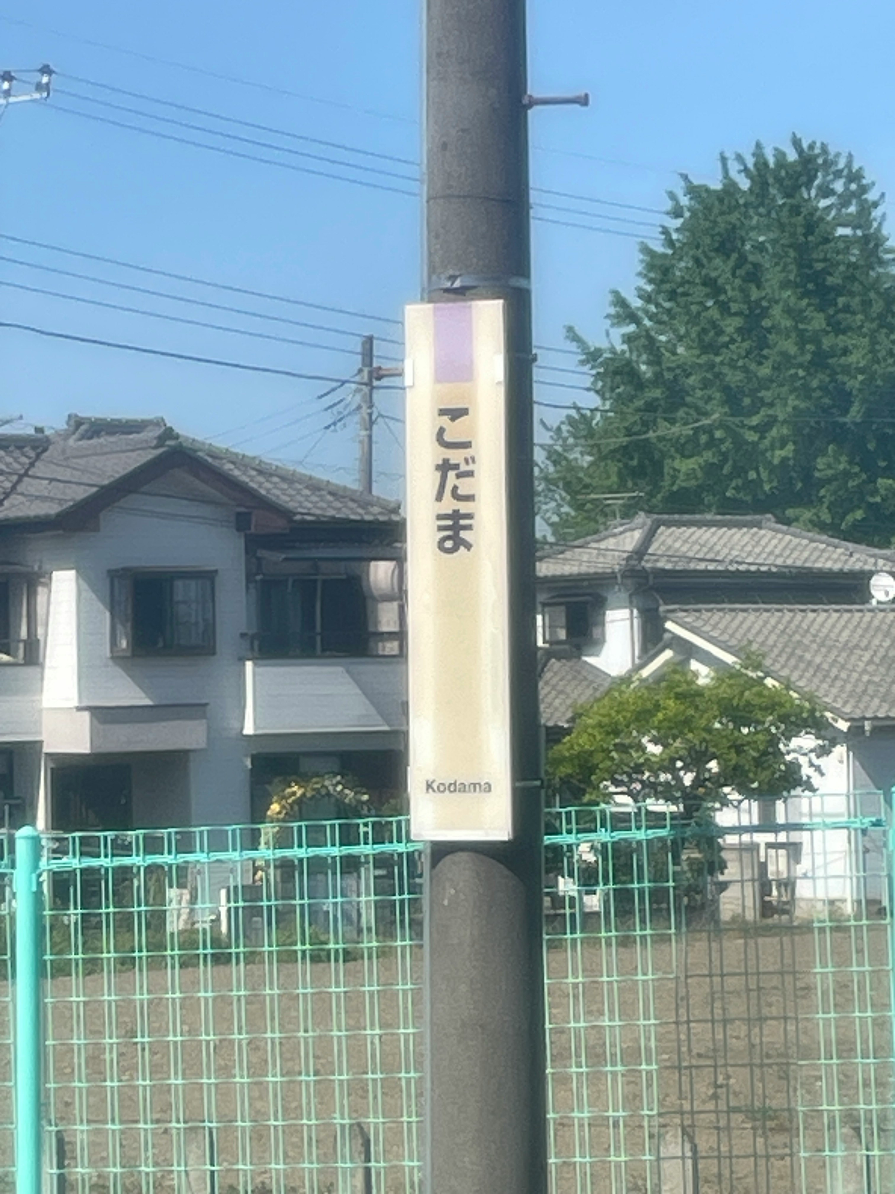 「こだま」駅名標のある住宅街のフェンス前