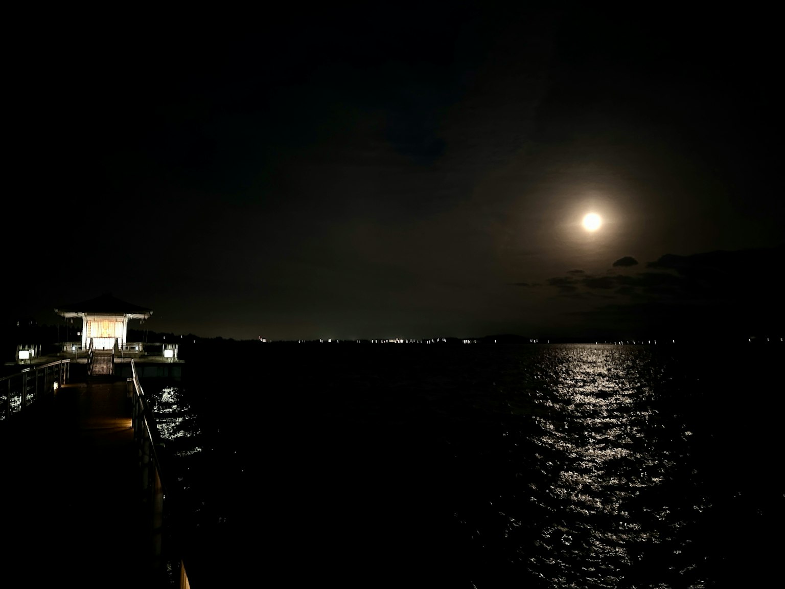Scena notturna con la luce della luna che si riflette sull'acqua e una costa lontana