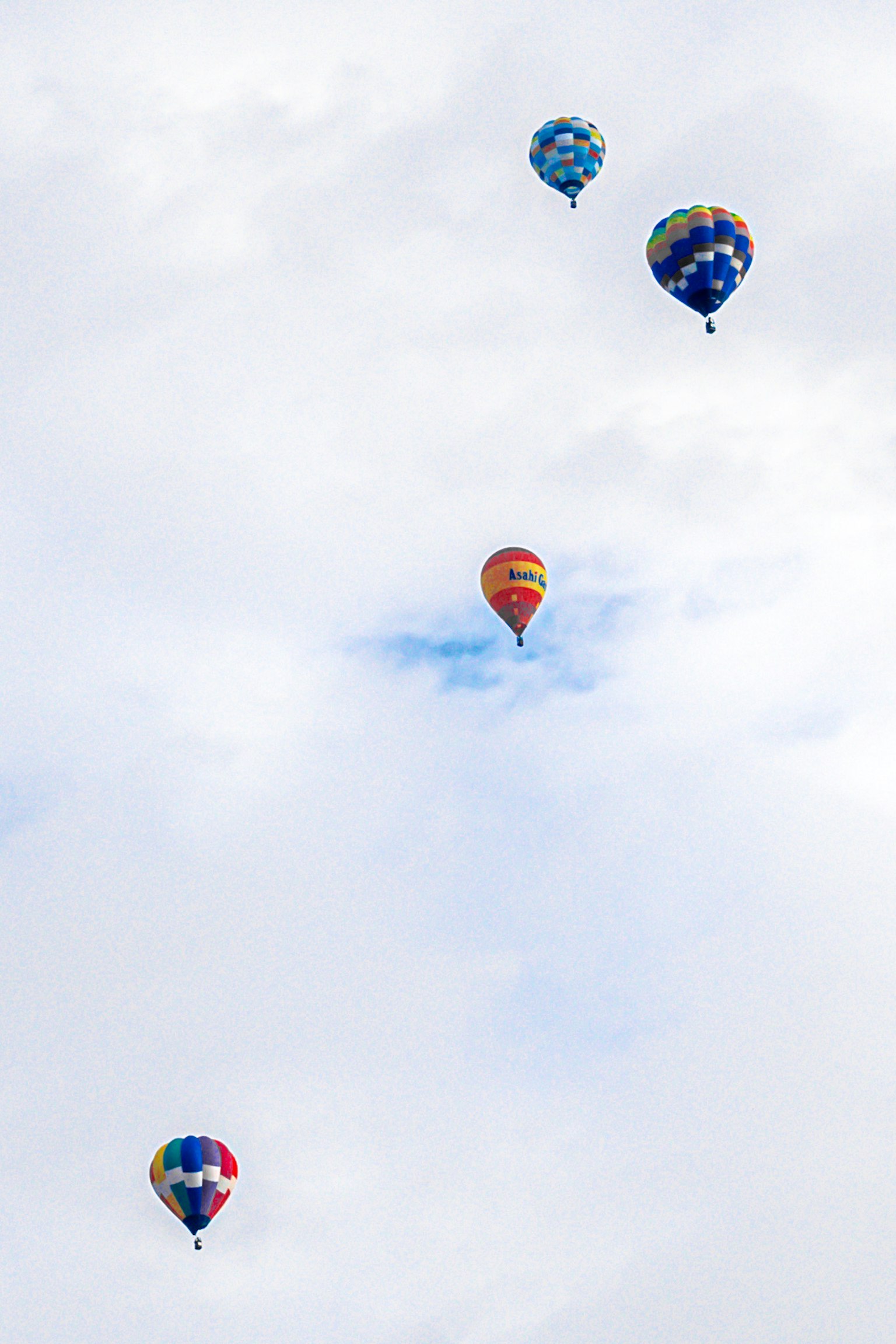 Empat balon udara panas berwarna-warni mengapung di langit biru