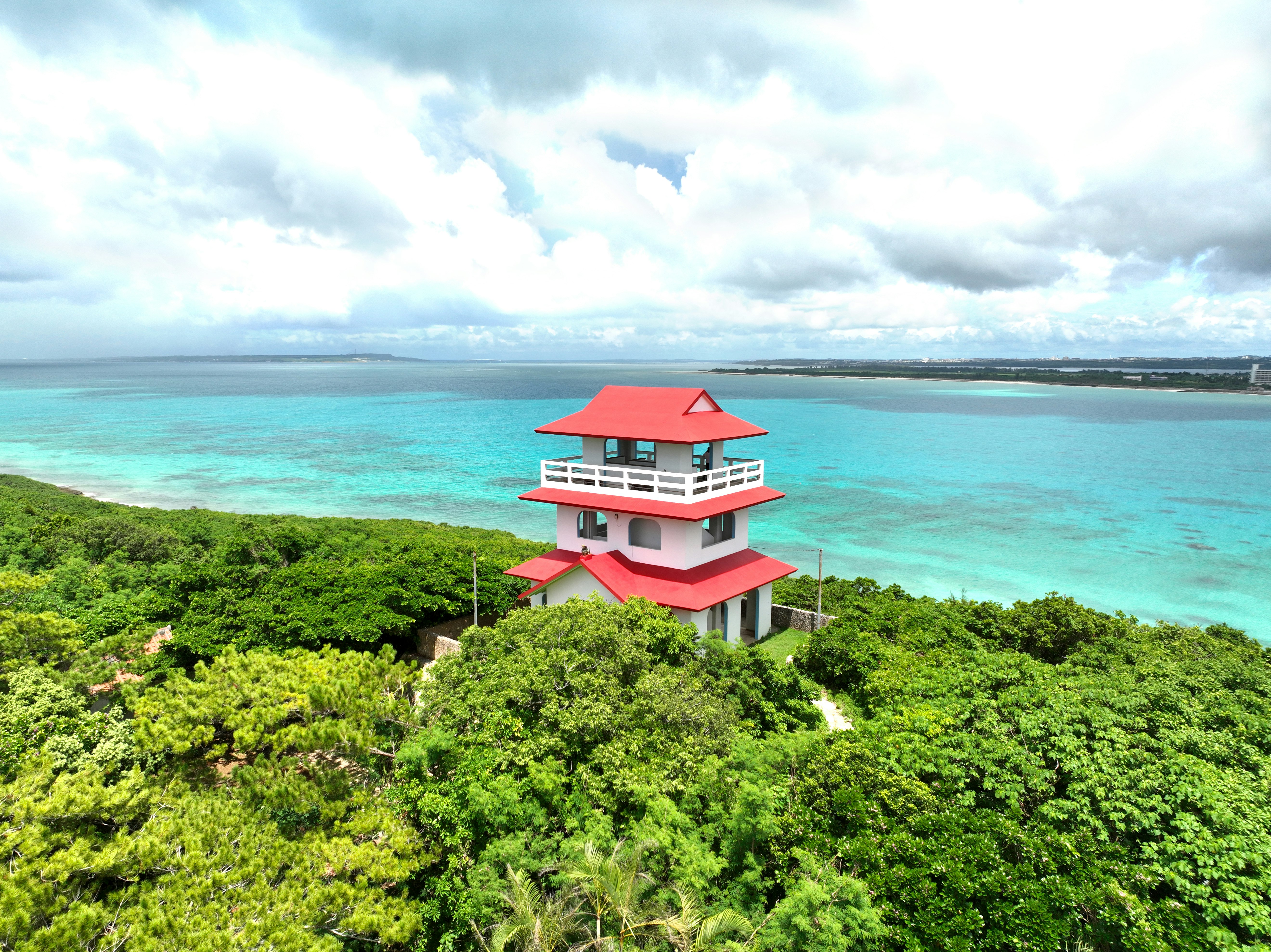 A red-roofed lighthouse surrounded by green trees and blue ocean