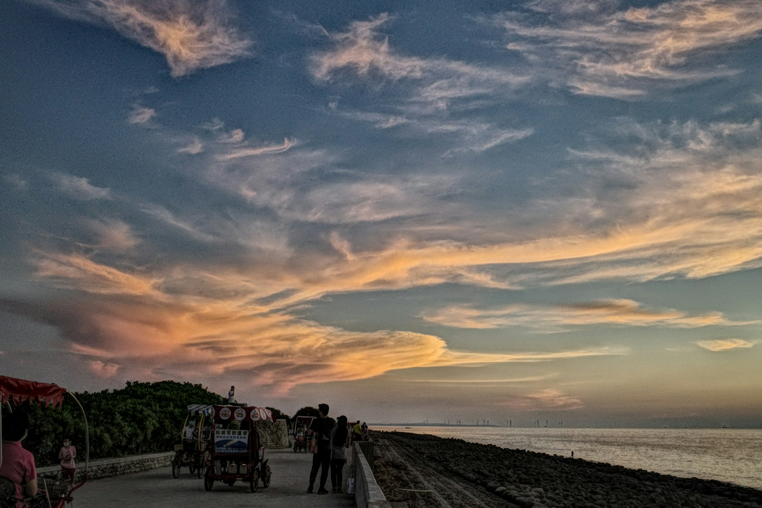 夕焼けの空と海岸沿いの散歩道を歩く人々