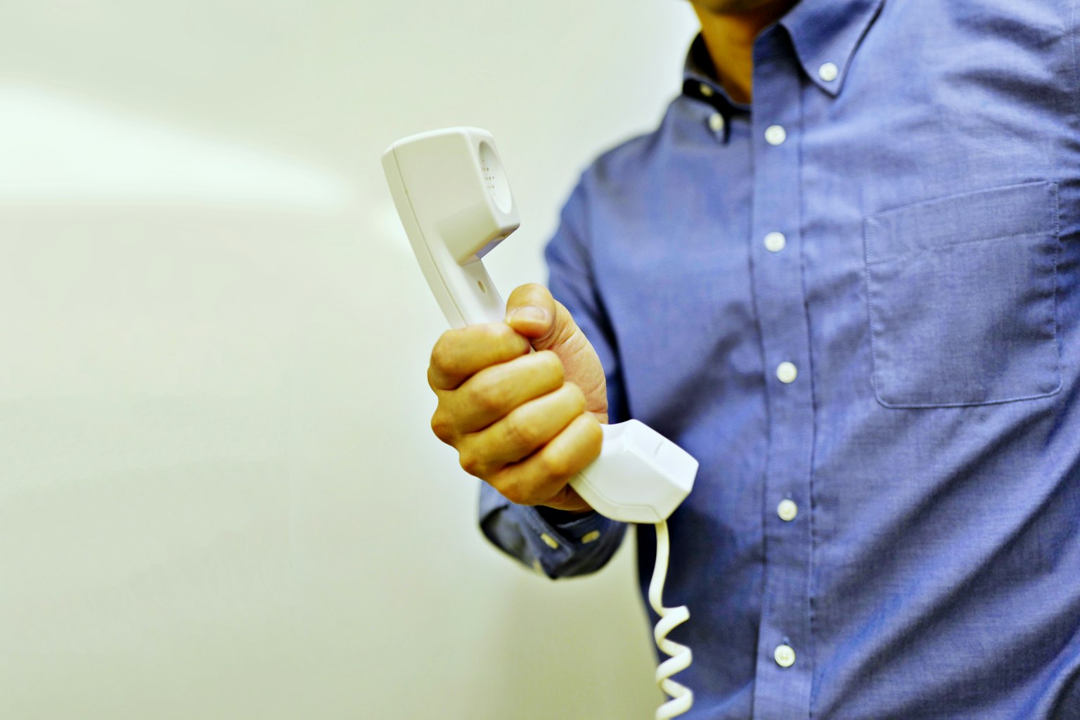 Nahaufnahme einer Hand eines Mannes, die einen weißen Telefonhörer hält