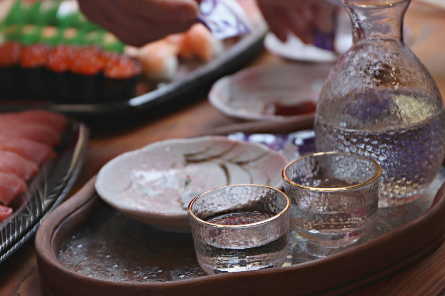 Una hermosa disposición de comida japonesa con copas de sake y una jarra, con sushi y sashimi al fondo