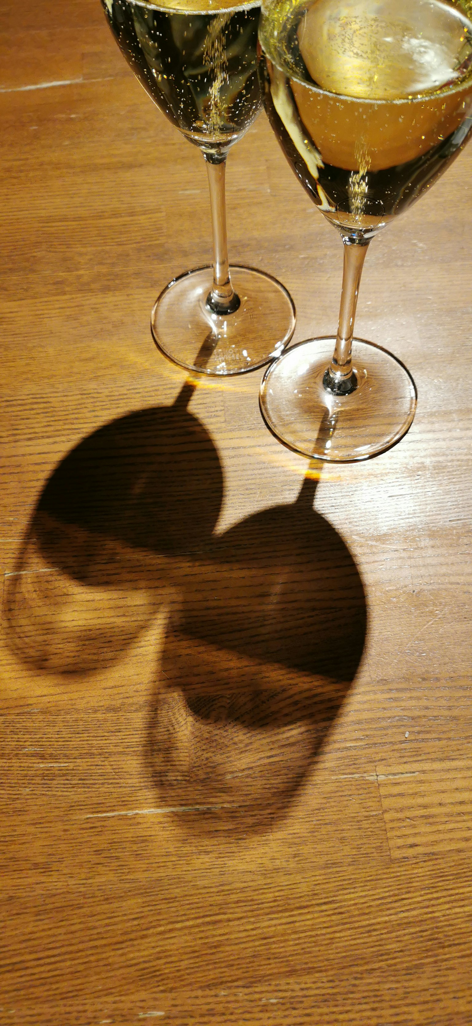 Two champagne glasses on a wooden table casting heart-shaped shadows