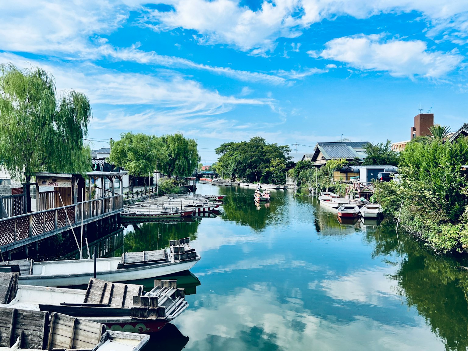 Aguas serenas que reflejan cielos azules y nubes blancas con botes alineados a lo largo de la ribera