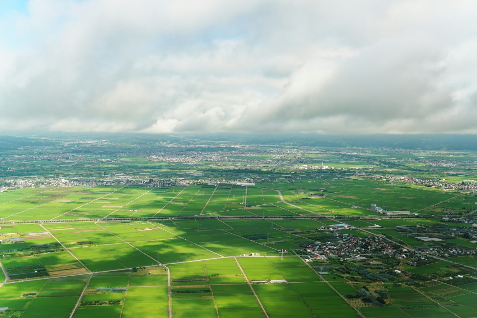 Vue aérienne de vastes terres agricoles vertes sous un ciel nuageux
