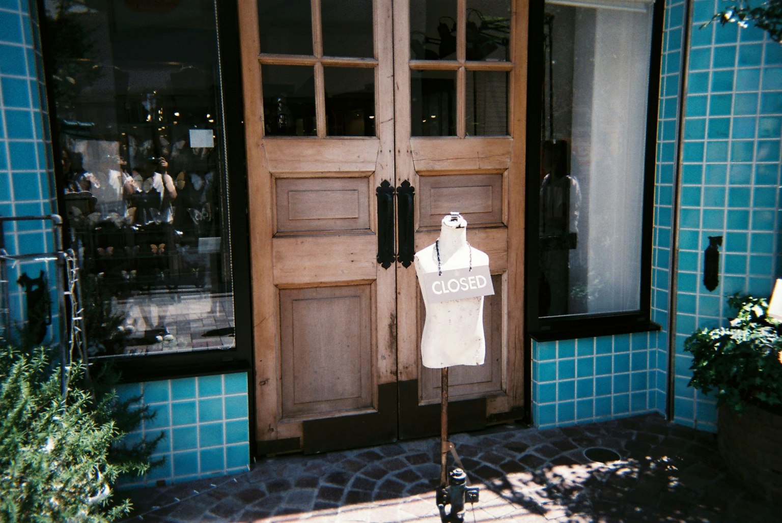 A mannequin stands in front of a shop with wooden doors and blue tiled exterior