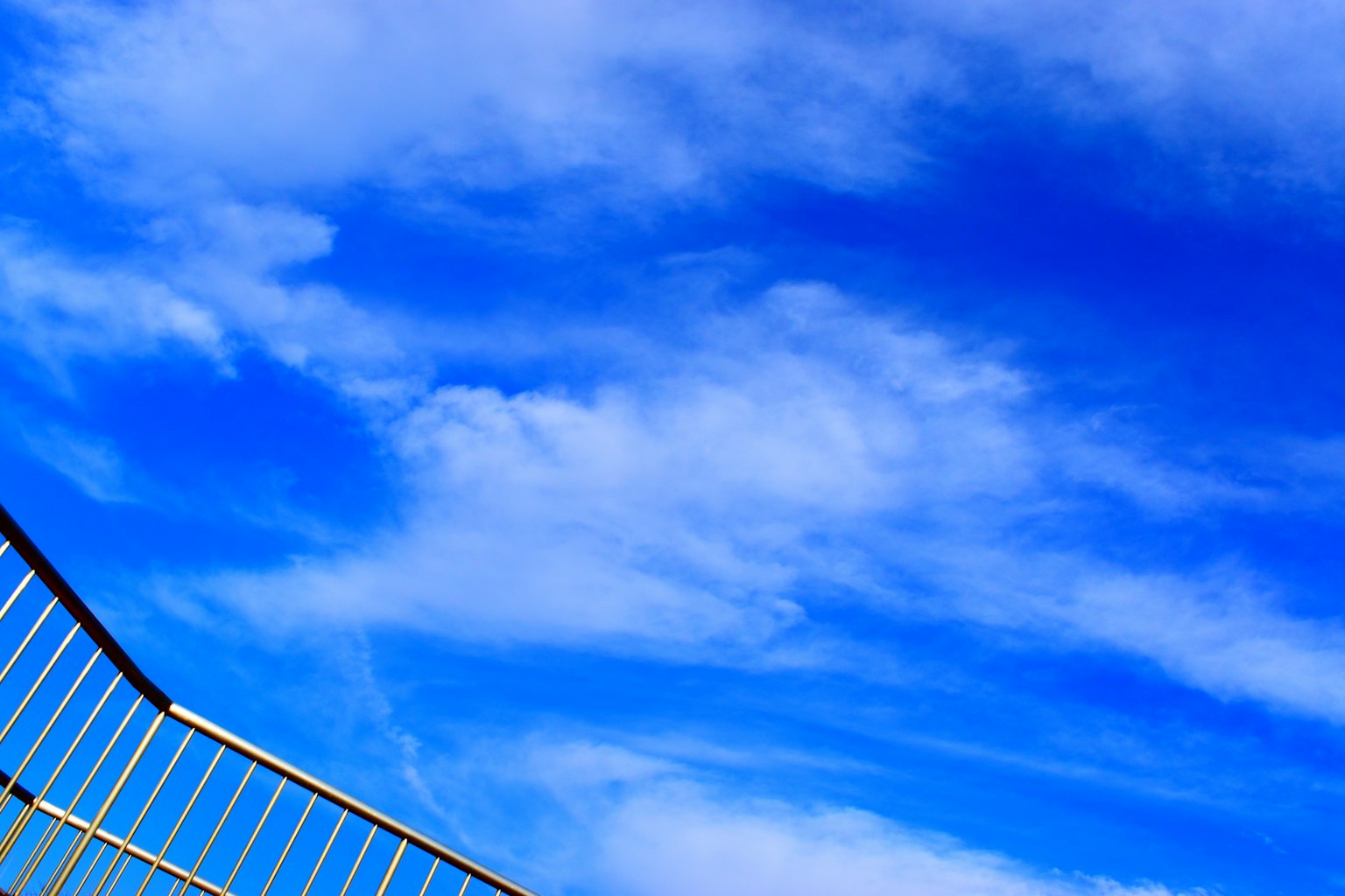Una hermosa vista del cielo azul con nubes blancas y una barandilla metálica