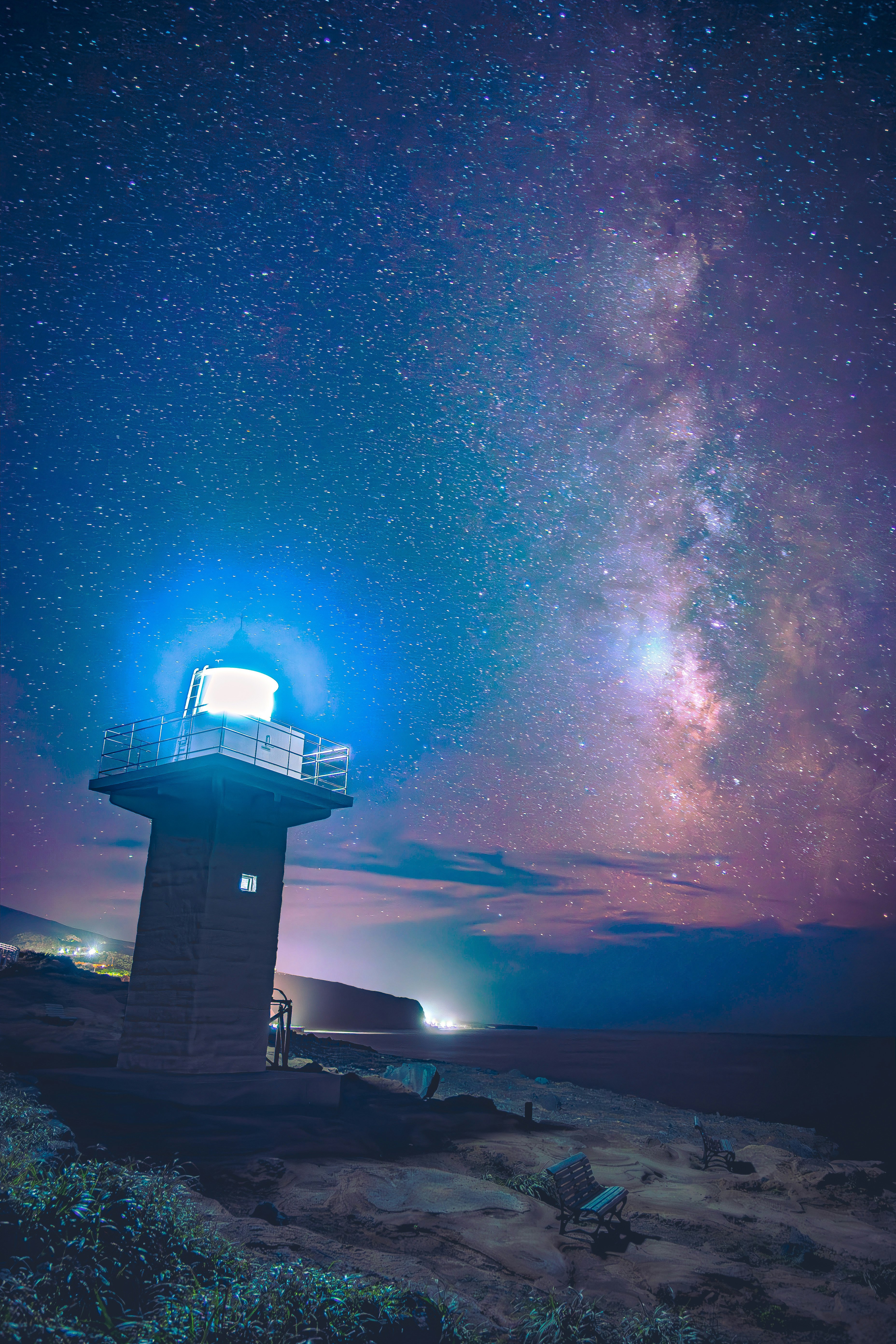 灯台と満天の星空が広がる海辺の夜景