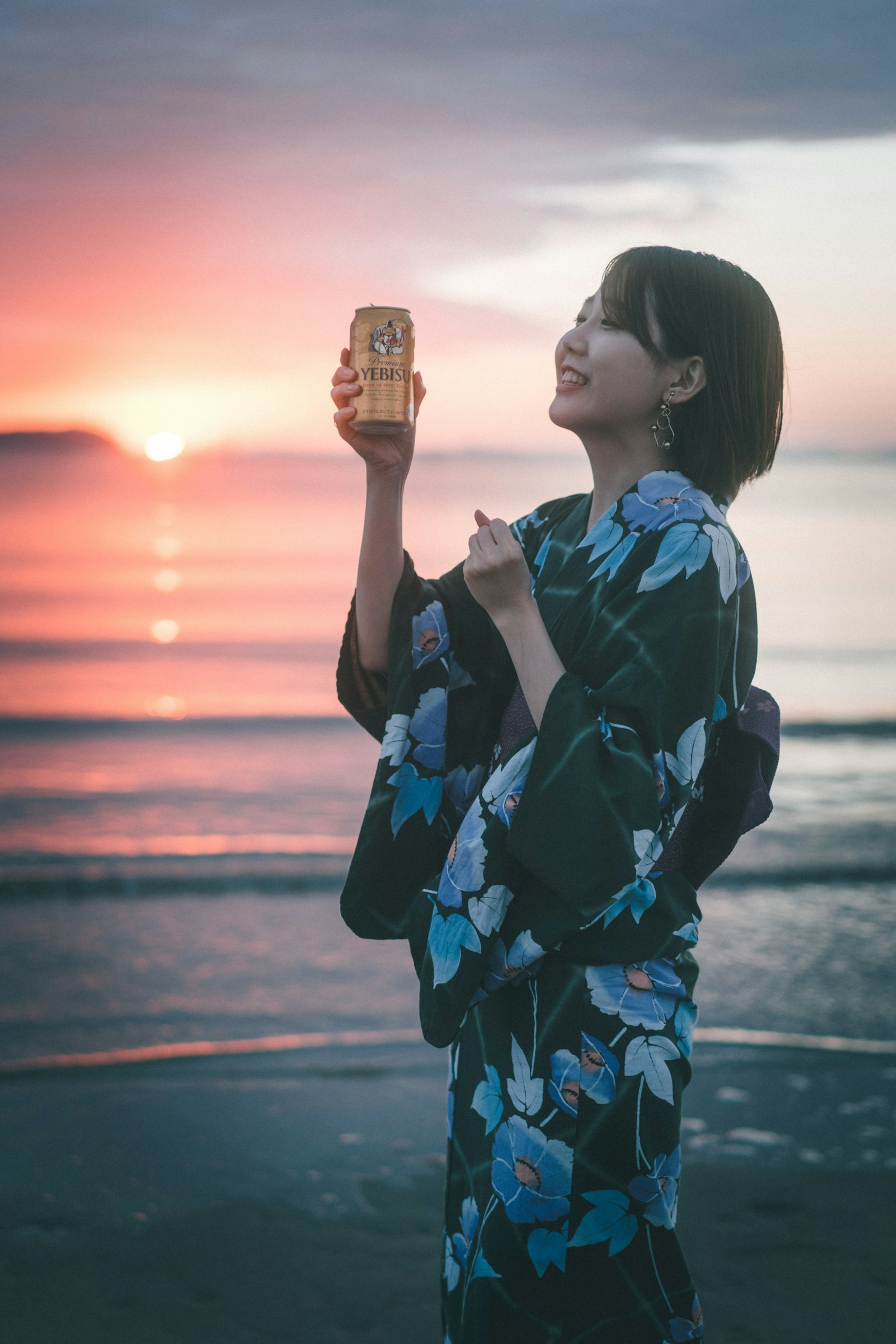 Una donna in yukata giapponese sorride mentre tiene qualcosa contro un bellissimo tramonto