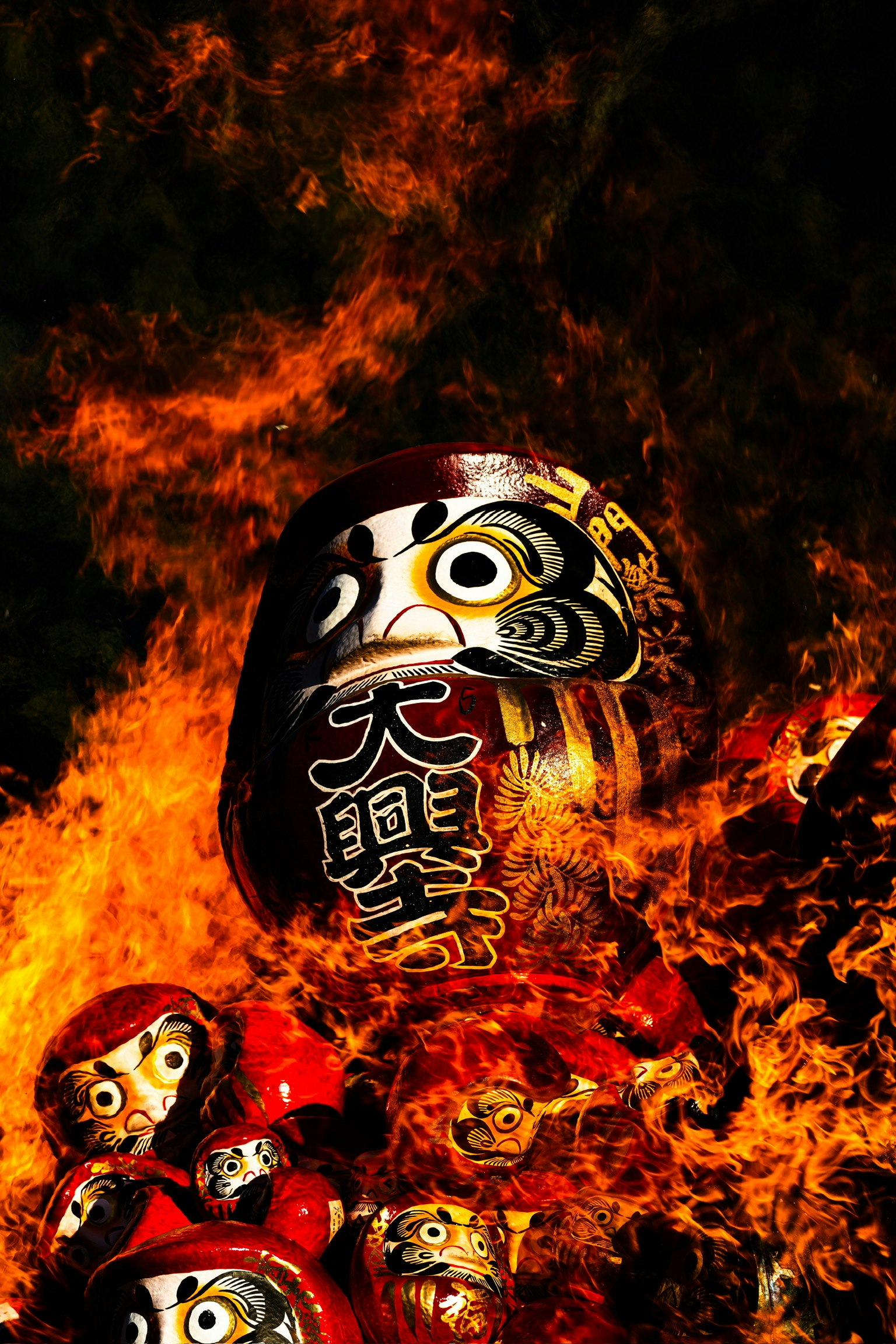 Gruppo di bambole Daruma circondate da fiamme con un grande volto di Daruma
