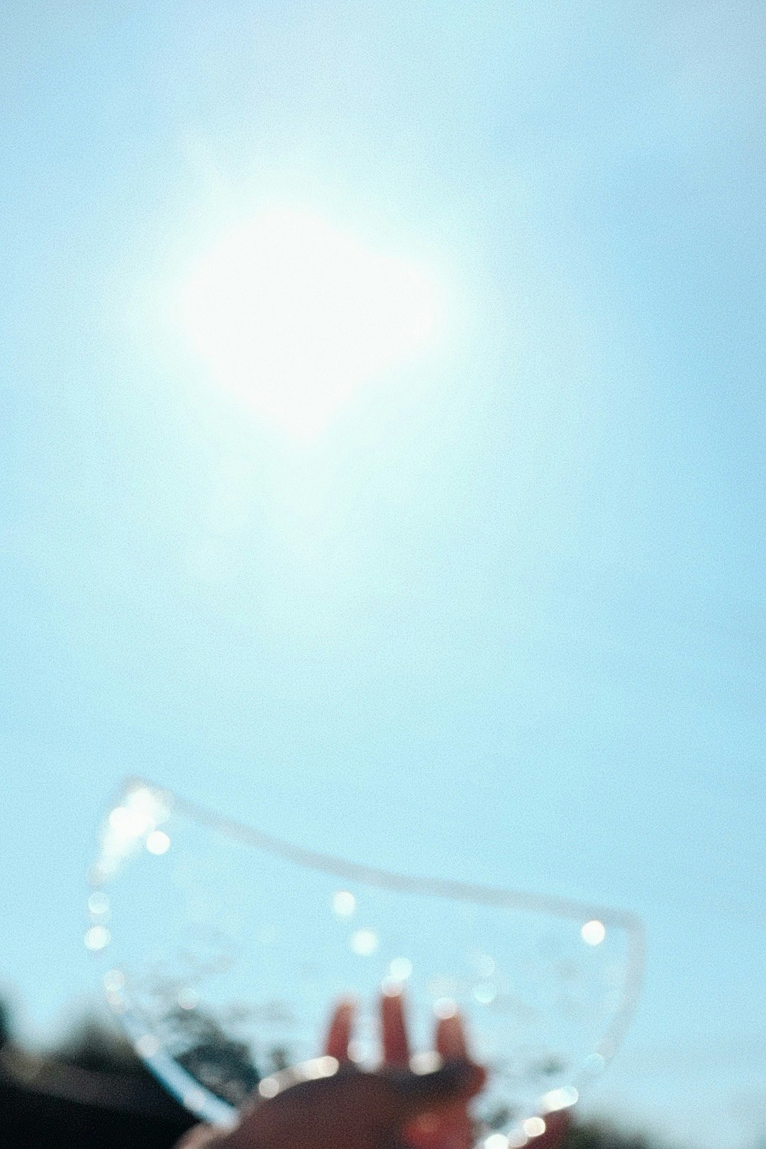 青空の下で手に持たれた透明な物体と太陽の光