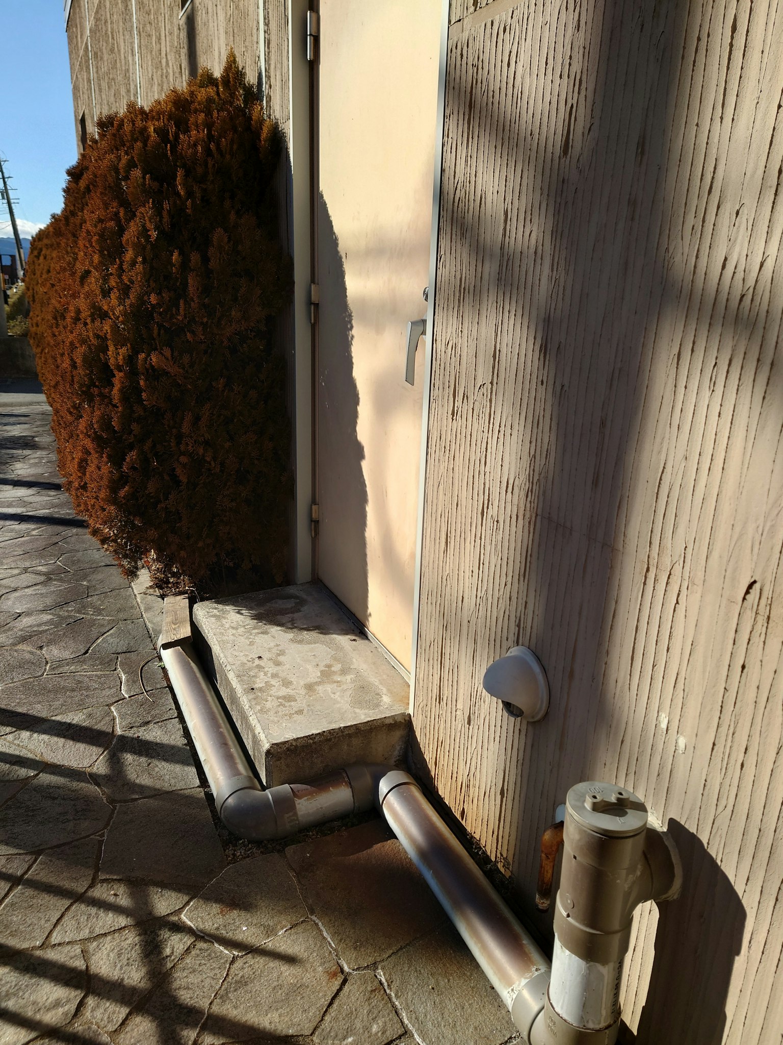 Escalón de concreto y tuberías cerca de una puerta en un entorno soleado