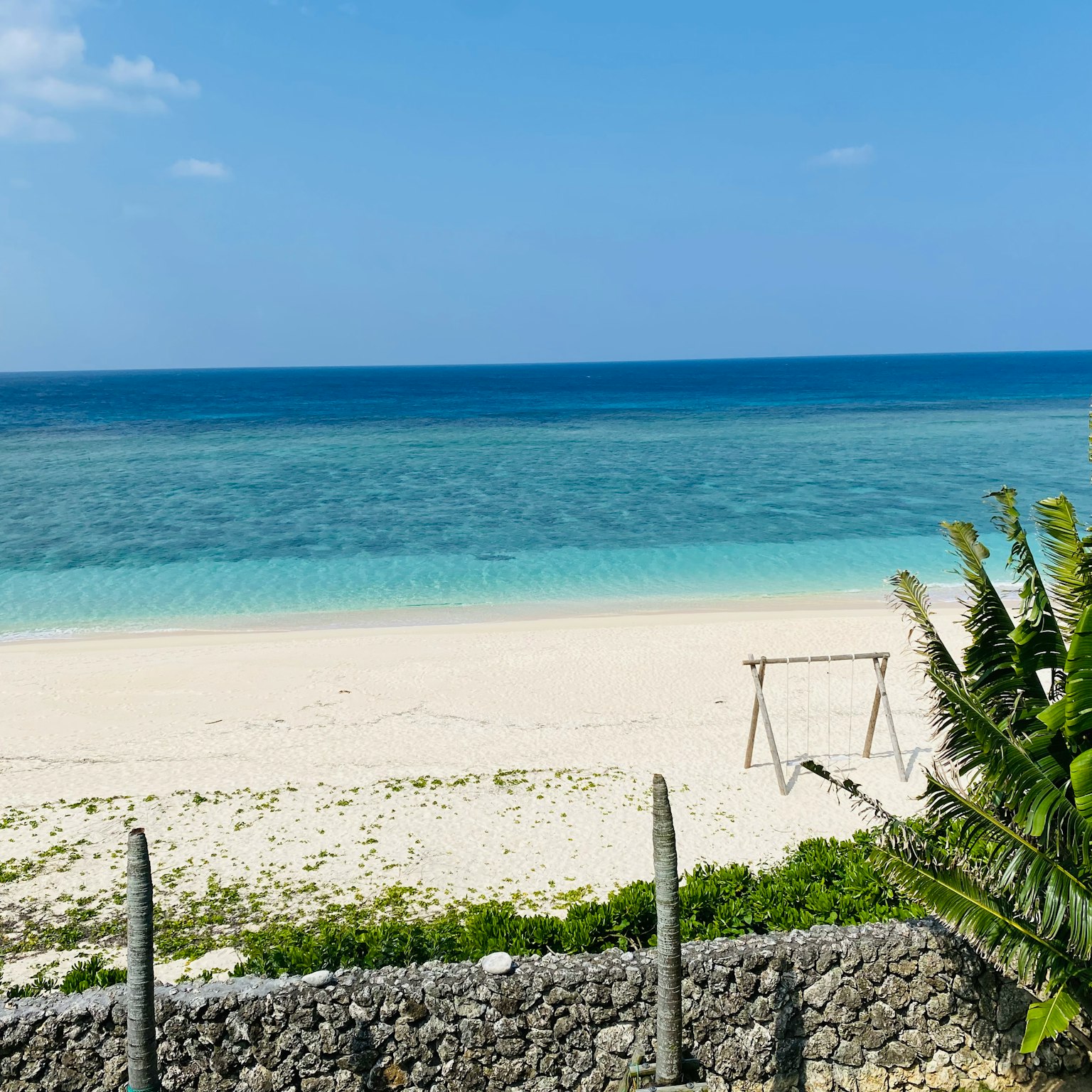 Scenic view of a beach with blue water and white sand featuring a swing