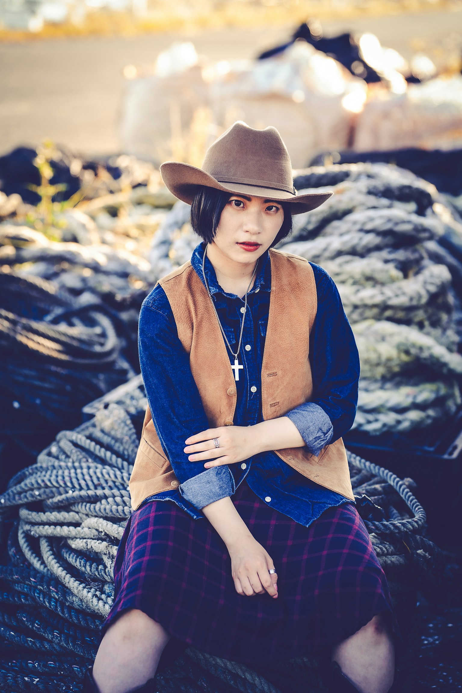 A woman wearing a cowboy hat and denim shirt sits on a pile of ropes