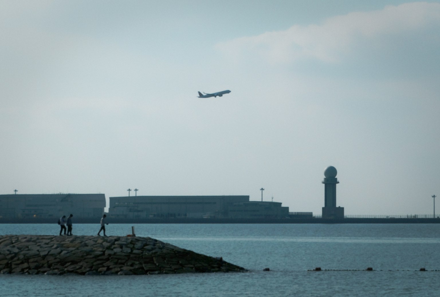 A plane taking off over the water with a lighthouse and people on a small island