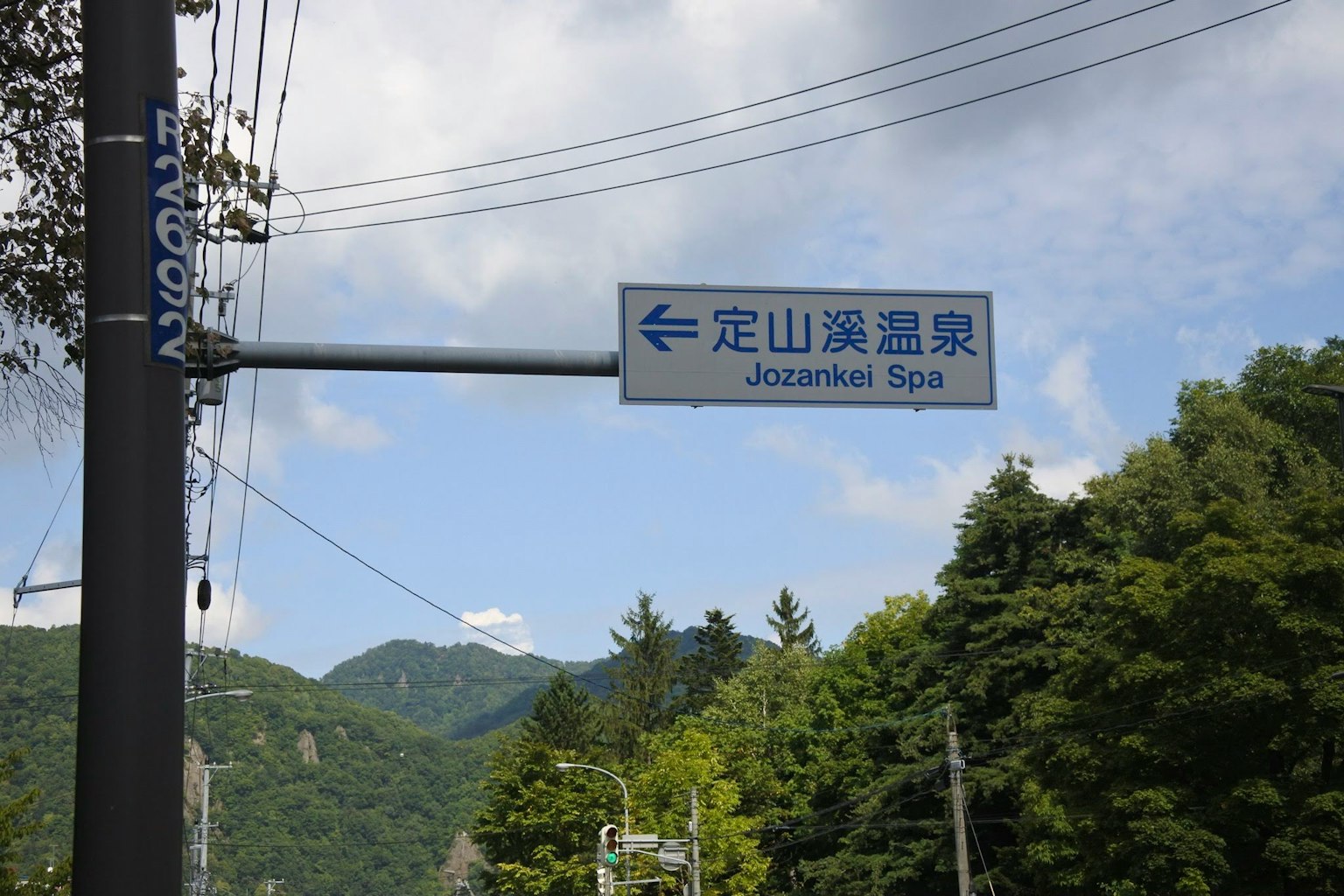 指向日本溫泉的標誌，周圍環繞著山脈和綠樹