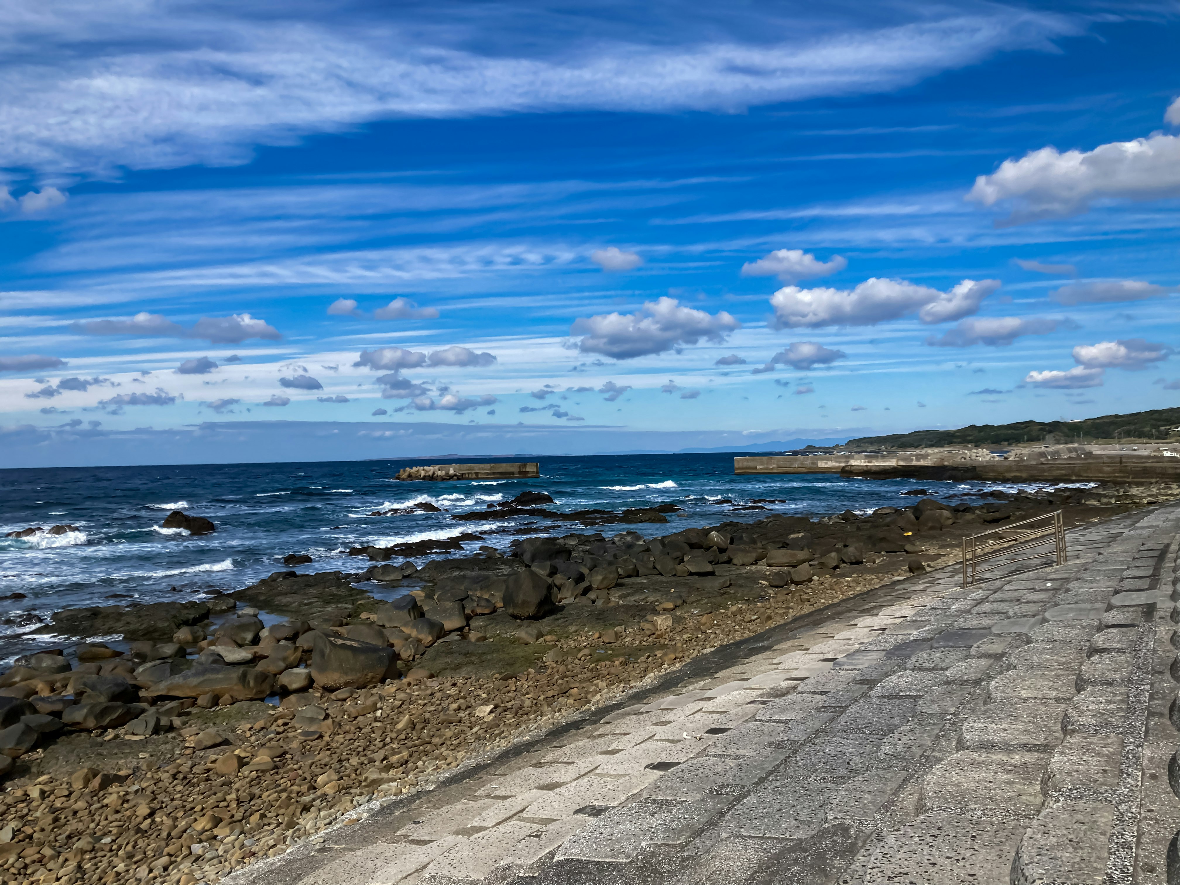 Seaside promenade along rocky shoreline under a blue sky