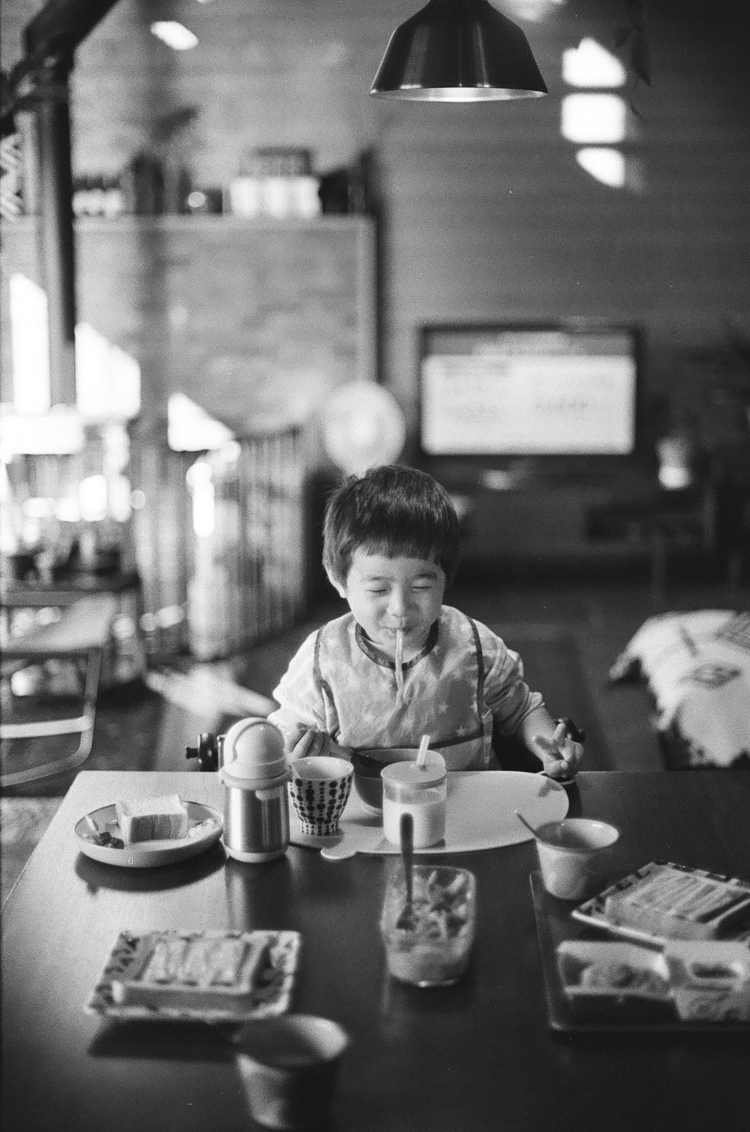 Photo en noir et blanc d'un enfant assis à une table avec de la nourriture et des boissons