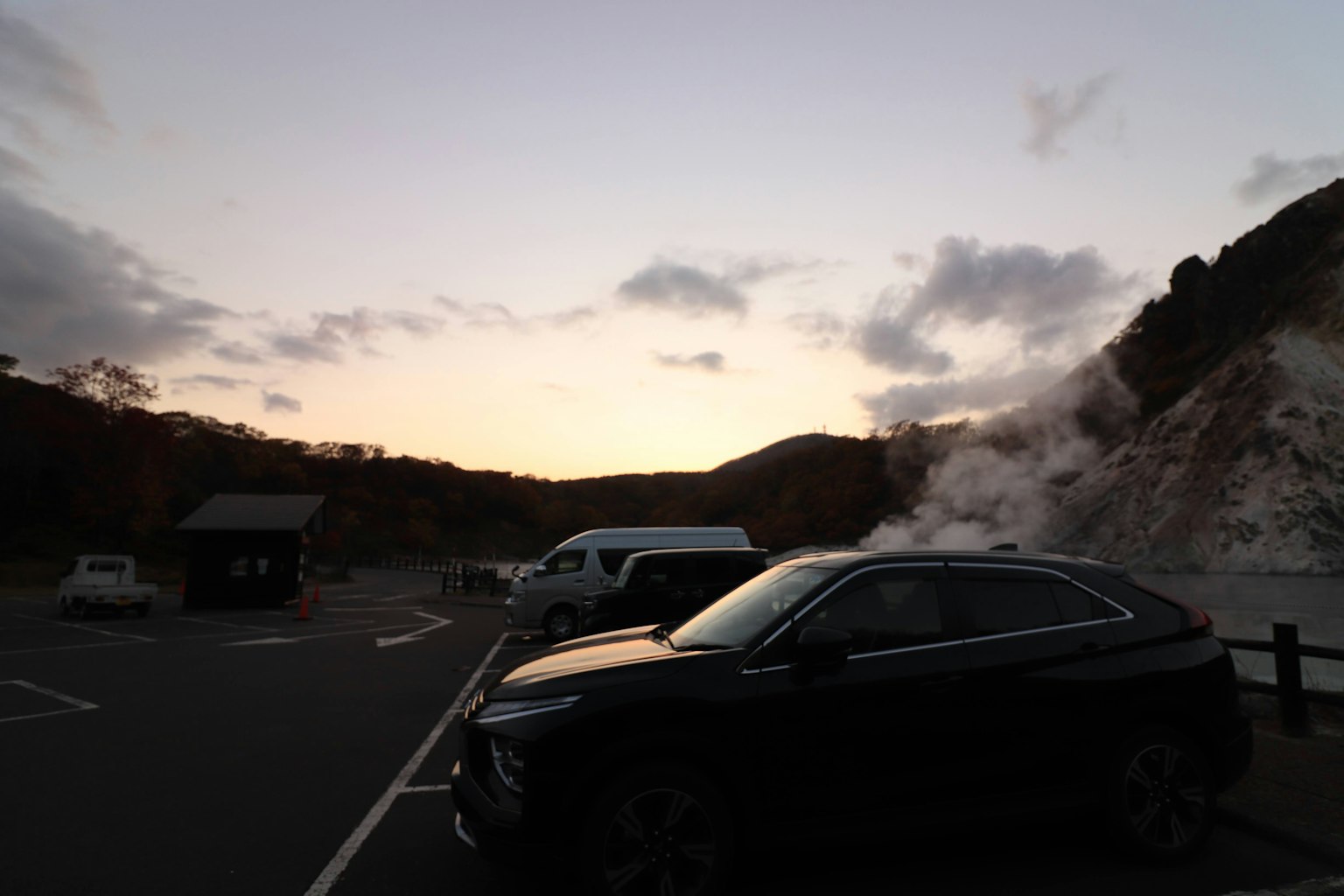 日落時停在停車場的黑色SUV，熱泉冒出的蒸氣的輪廓