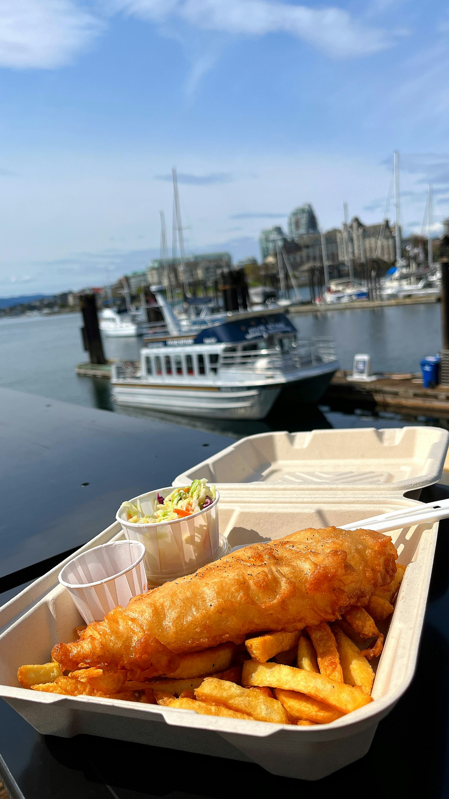 Un plato de pescado y papas fritas con vista al puerto de fondo