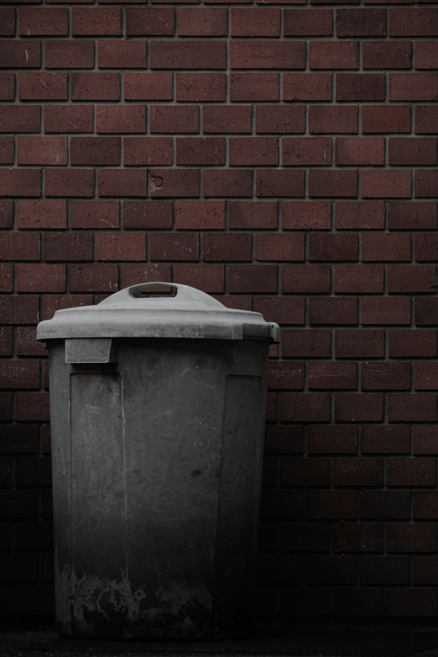 Un bidone della spazzatura grigio posizionato contro un muro di mattoni
