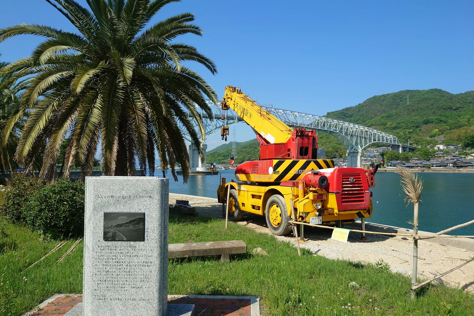 Une grue rouge et jaune garée au bord de la mer avec un palmier en arrière-plan