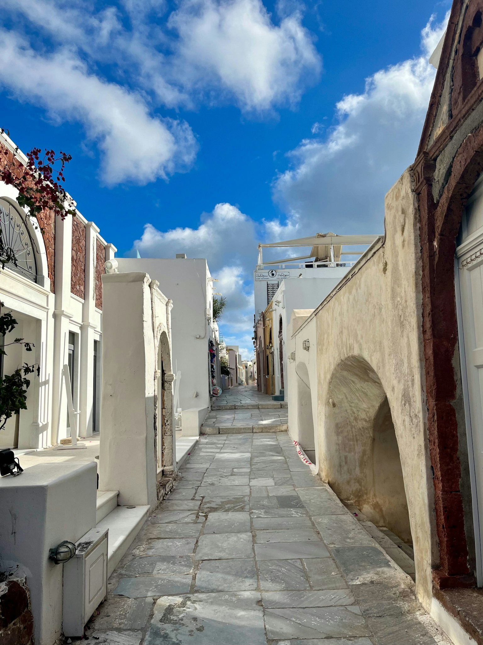 Calle estrecha en Santorini flanqueada por edificios blancos y cielo azul