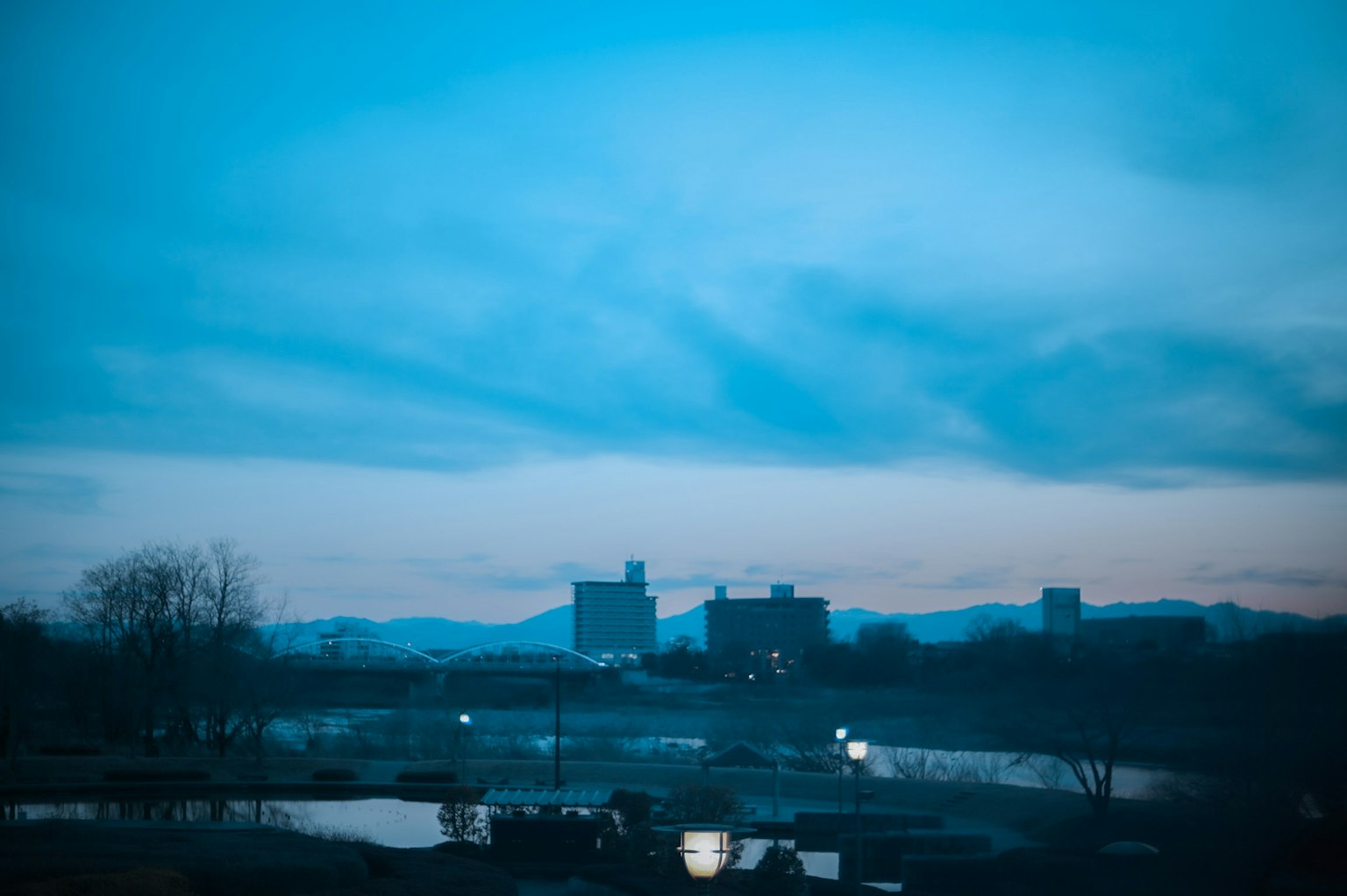 Paesaggio urbano con cielo blu e montagne sullo sfondo lago tranquillo al crepuscolo con silhouette della città