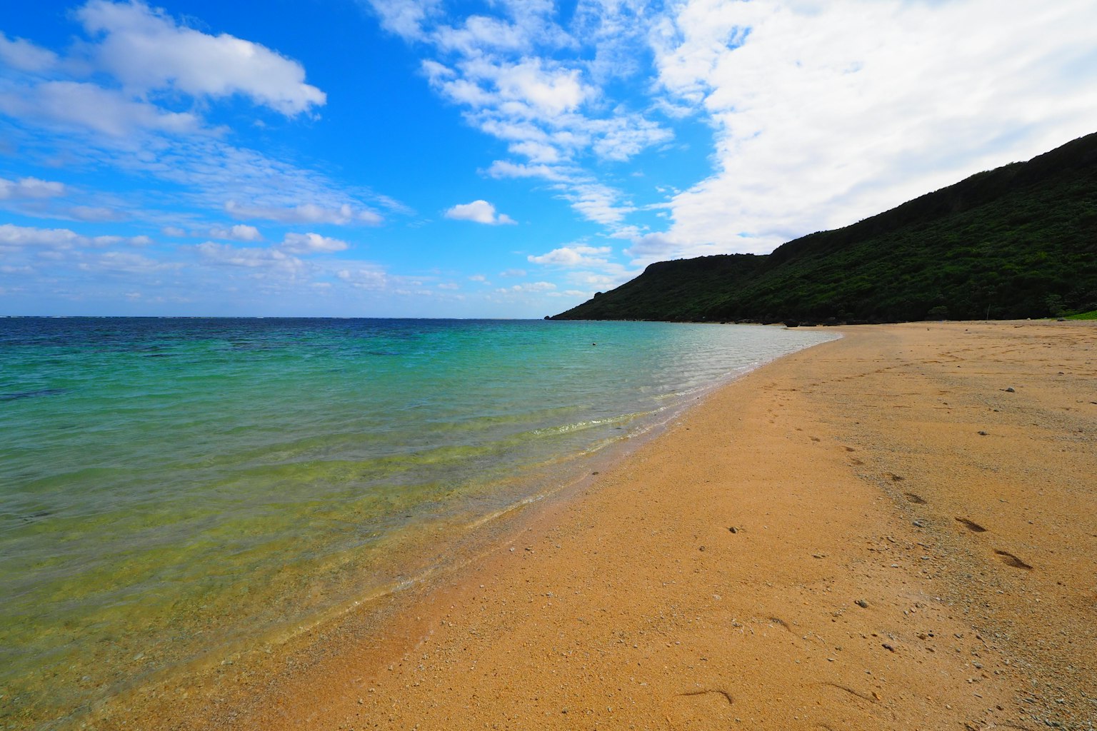 ทิวทัศน์ของมหาสมุทรสีน้ำเงินและชายหาดทรายพร้อมเนินเขาสีเขียวในพื้นหลัง