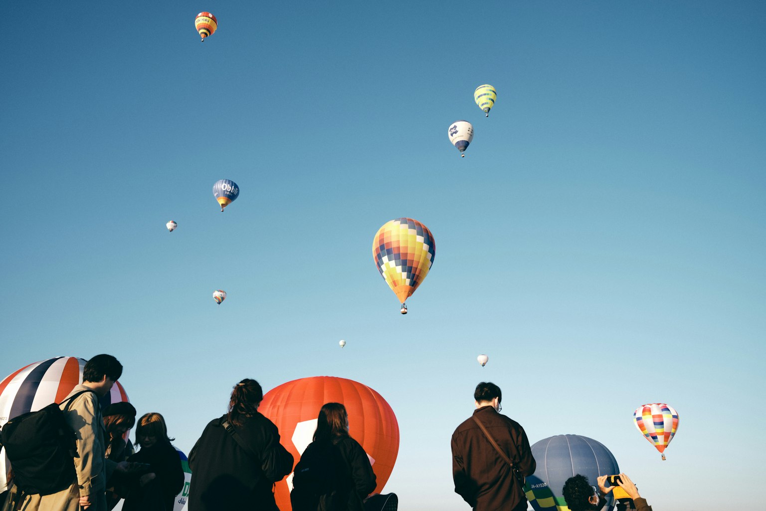 People watching hot air balloons flying in the blue sky