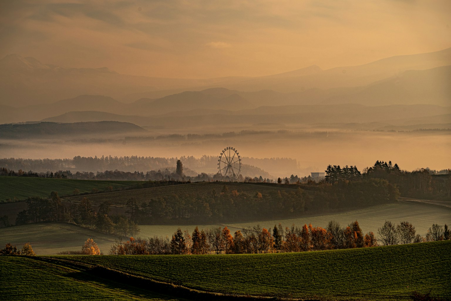 Paysage brumeux avec des collines ondulantes et une grande roue au loin en automne
