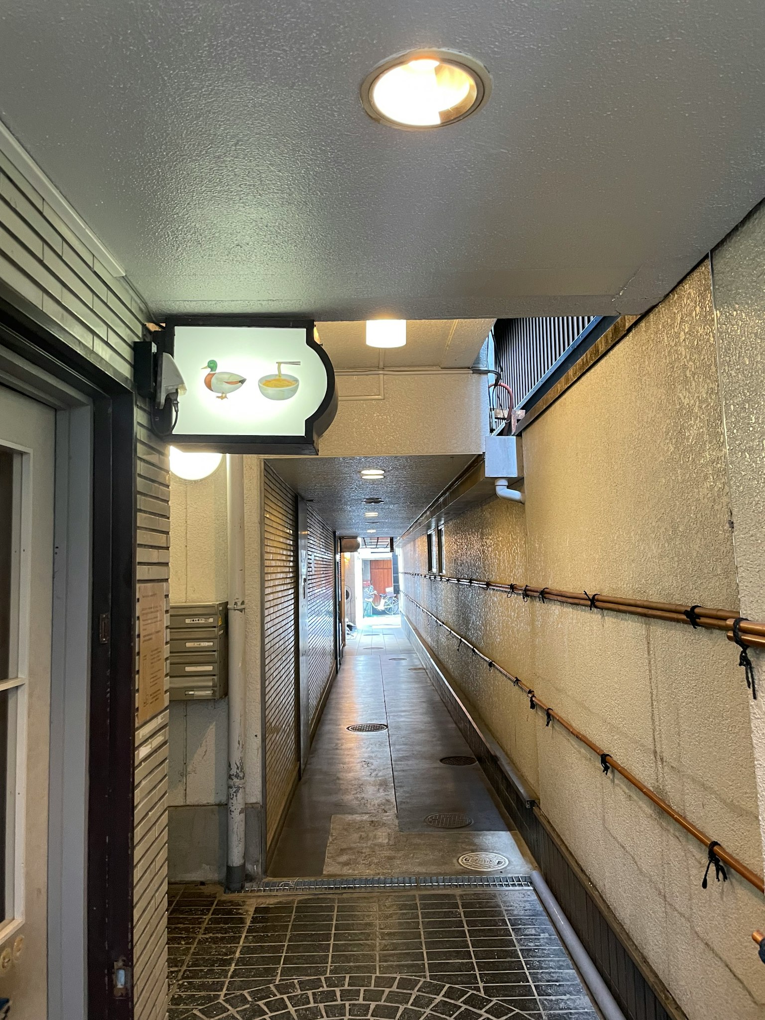 Narrow passageway leading to a bright exit with a sign