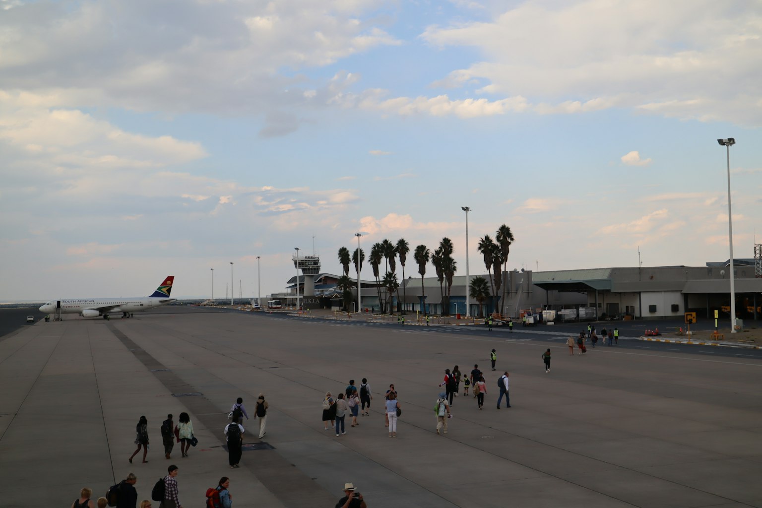 Airport runway with terminal and palm trees people walking