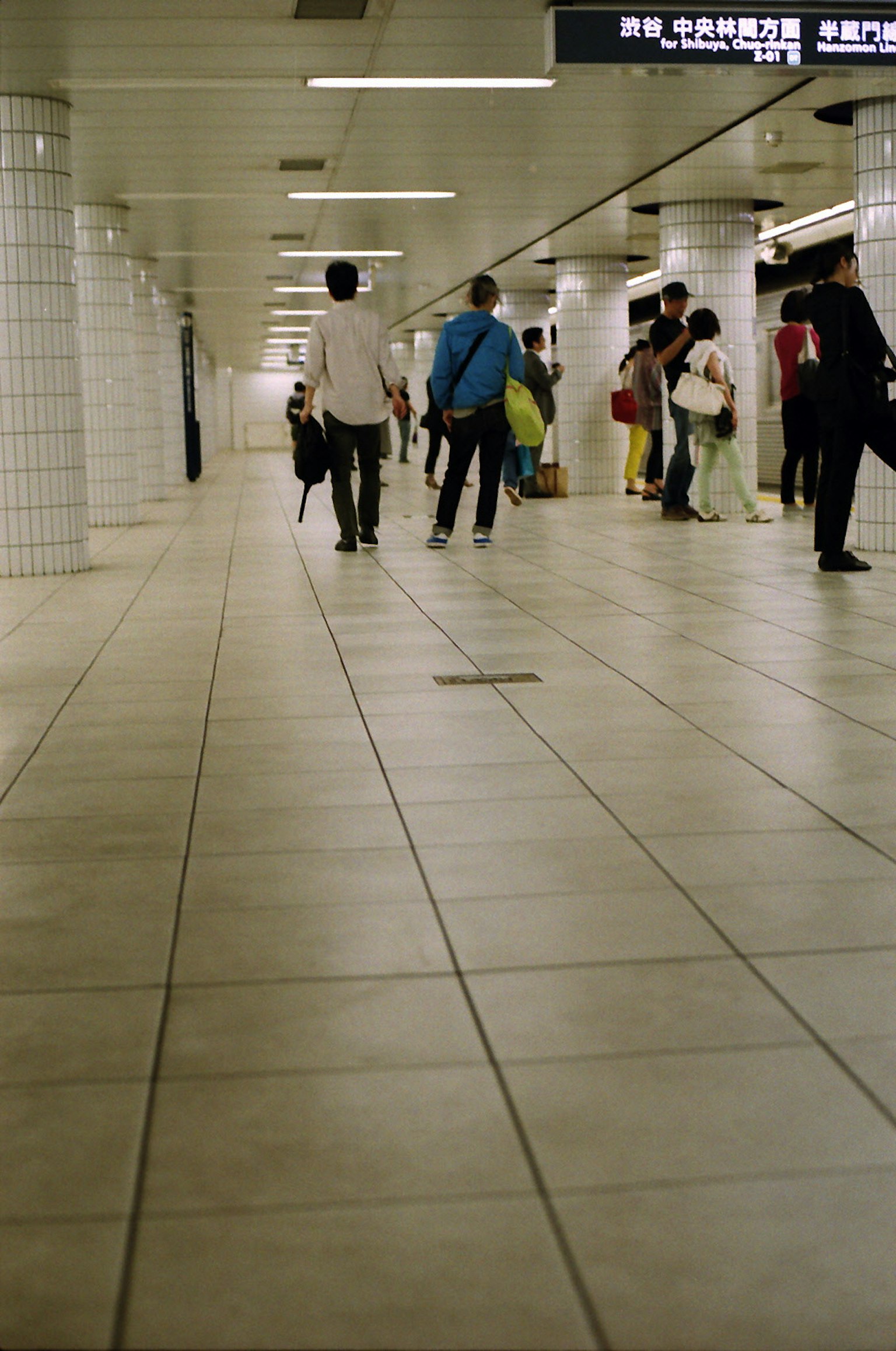 Personas caminando en un pasillo de estación de metro con piso de cerámica blanca