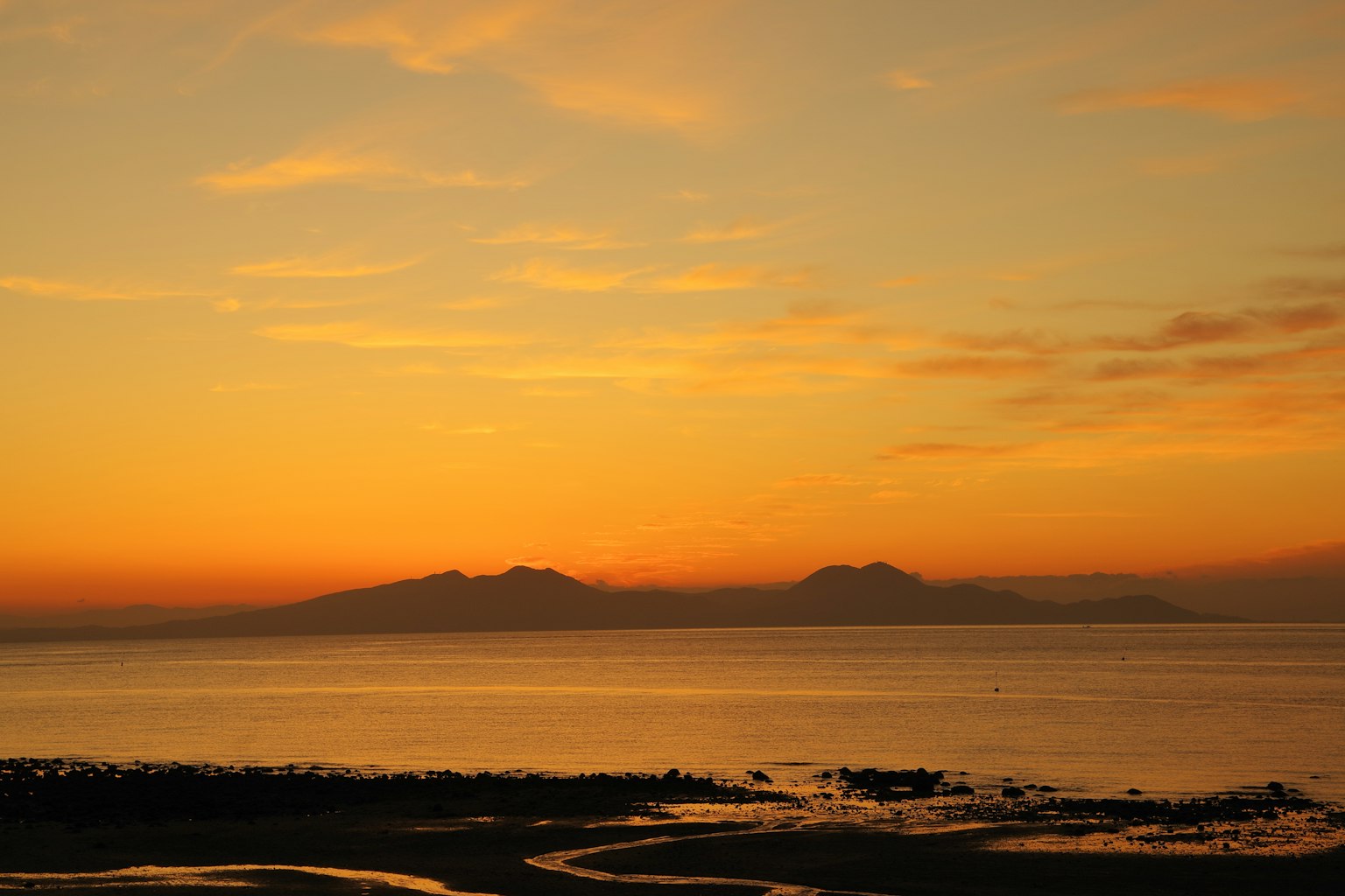 Tramonto sull'oceano con silhouette di montagne