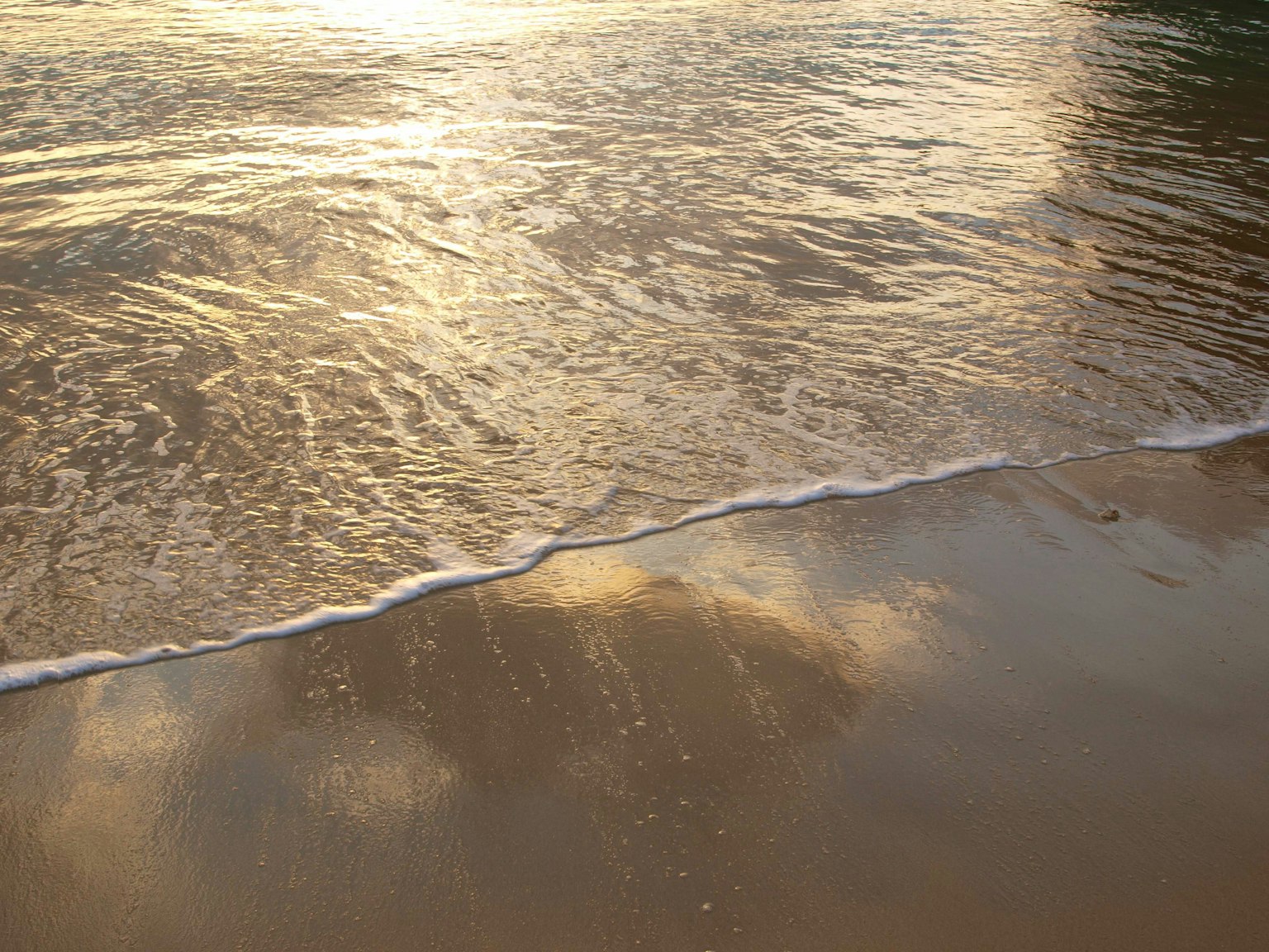 Sanfte Wellen brechen an einem Sandstrand im Abendlicht