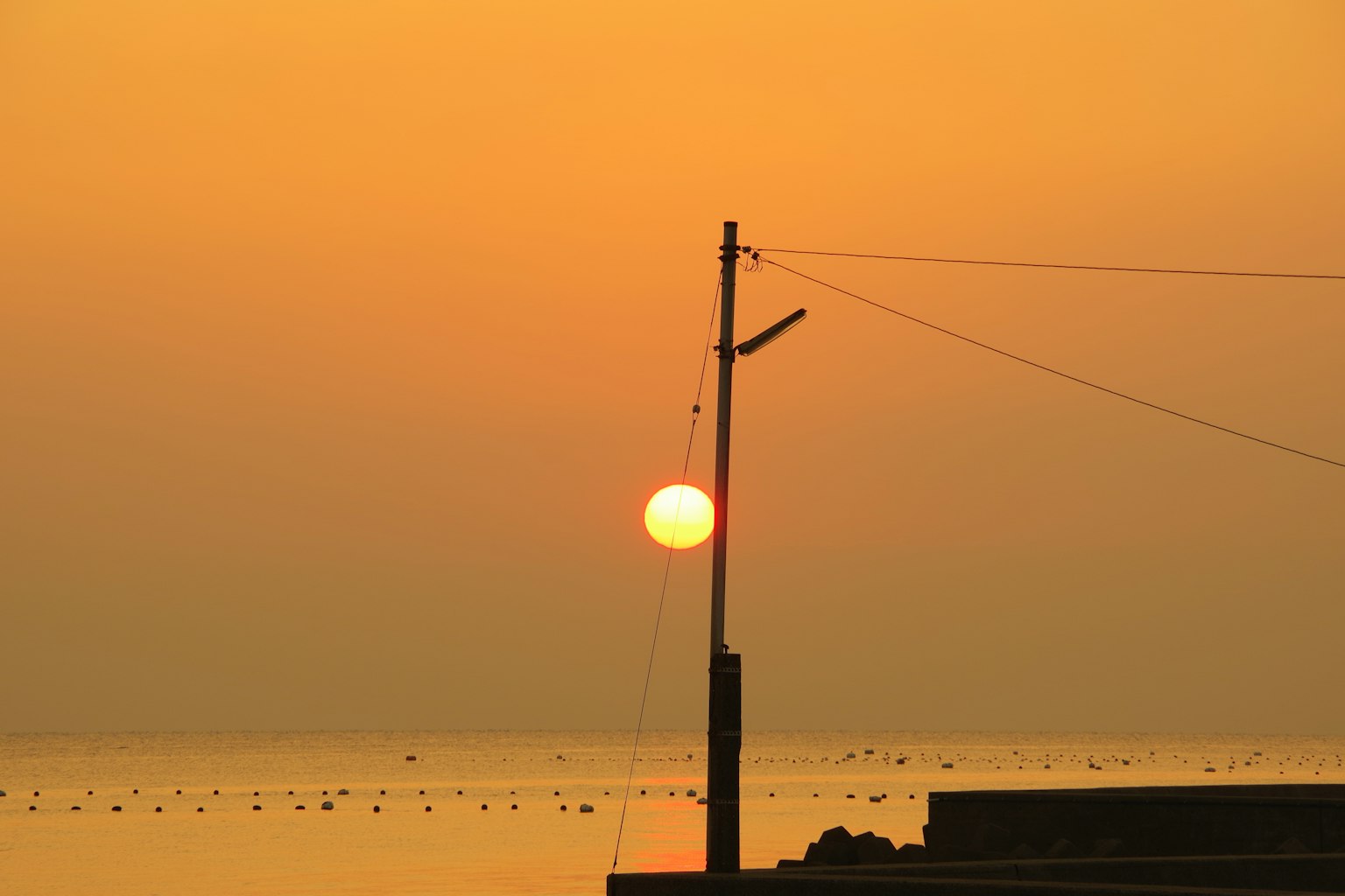 Sunset over the ocean with an orange sky and a utility pole