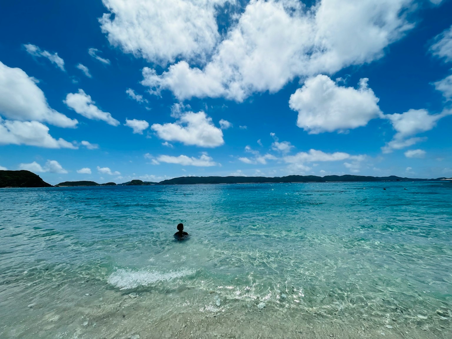 Une personne nageant dans une mer bleu clair sous un ciel ensoleillé avec des nuages blancs