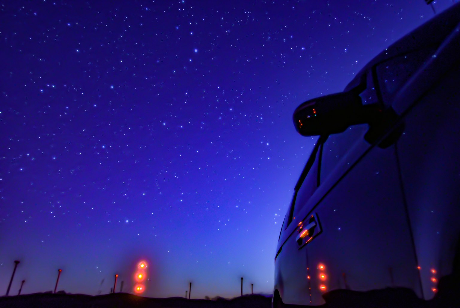 Una bellissima scena notturna con un cielo stellato e la silhouette di un'auto