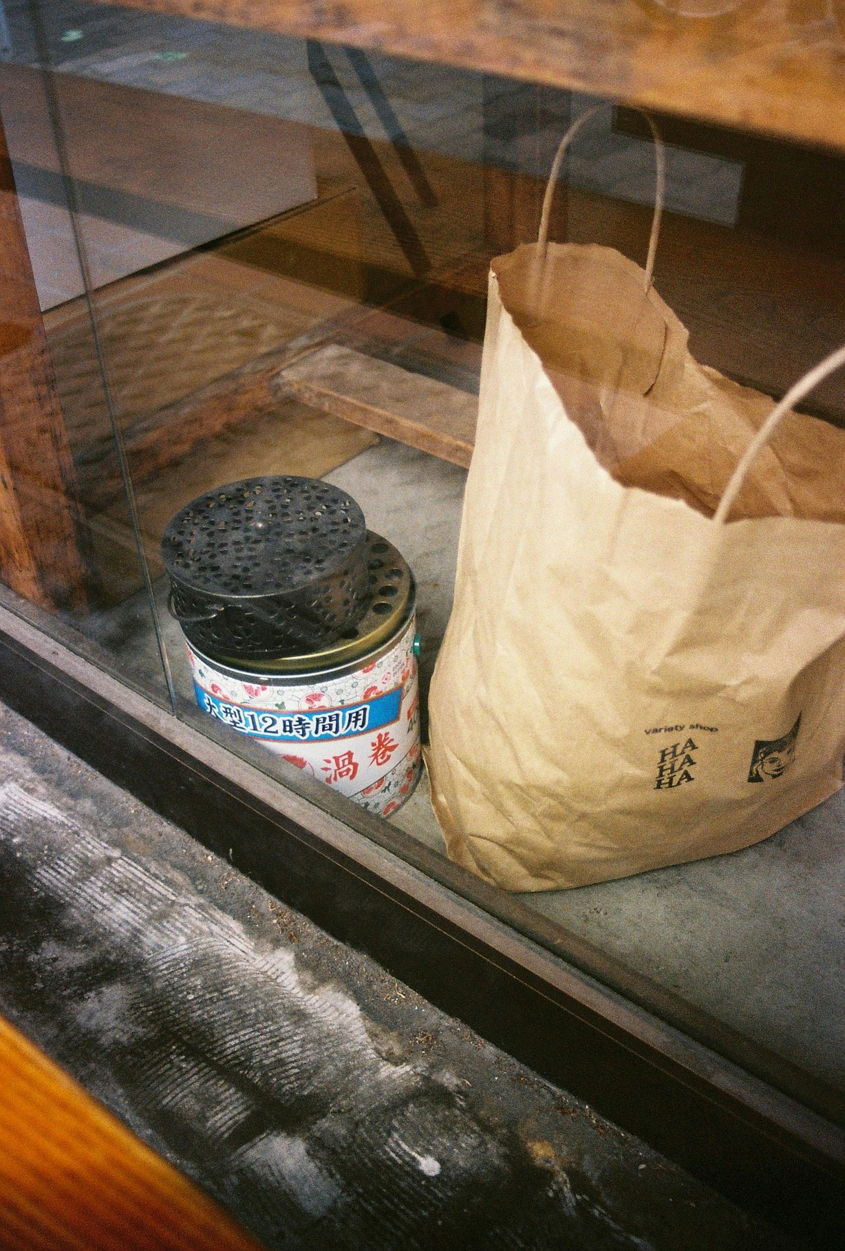 ガラス越しの紙袋と缶、店先の小物