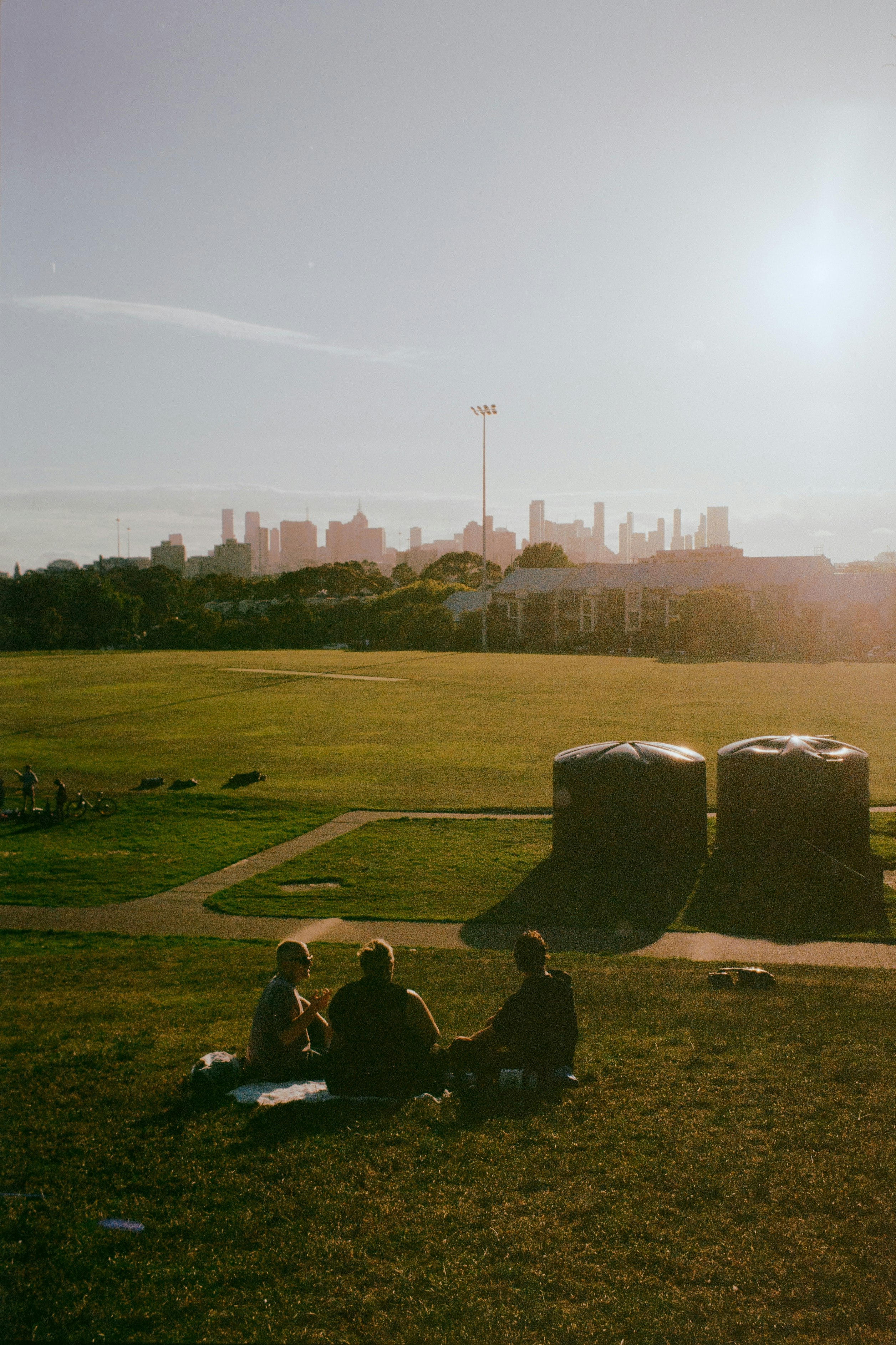 People relaxing on a park lawn at sunset with a downtown skyline