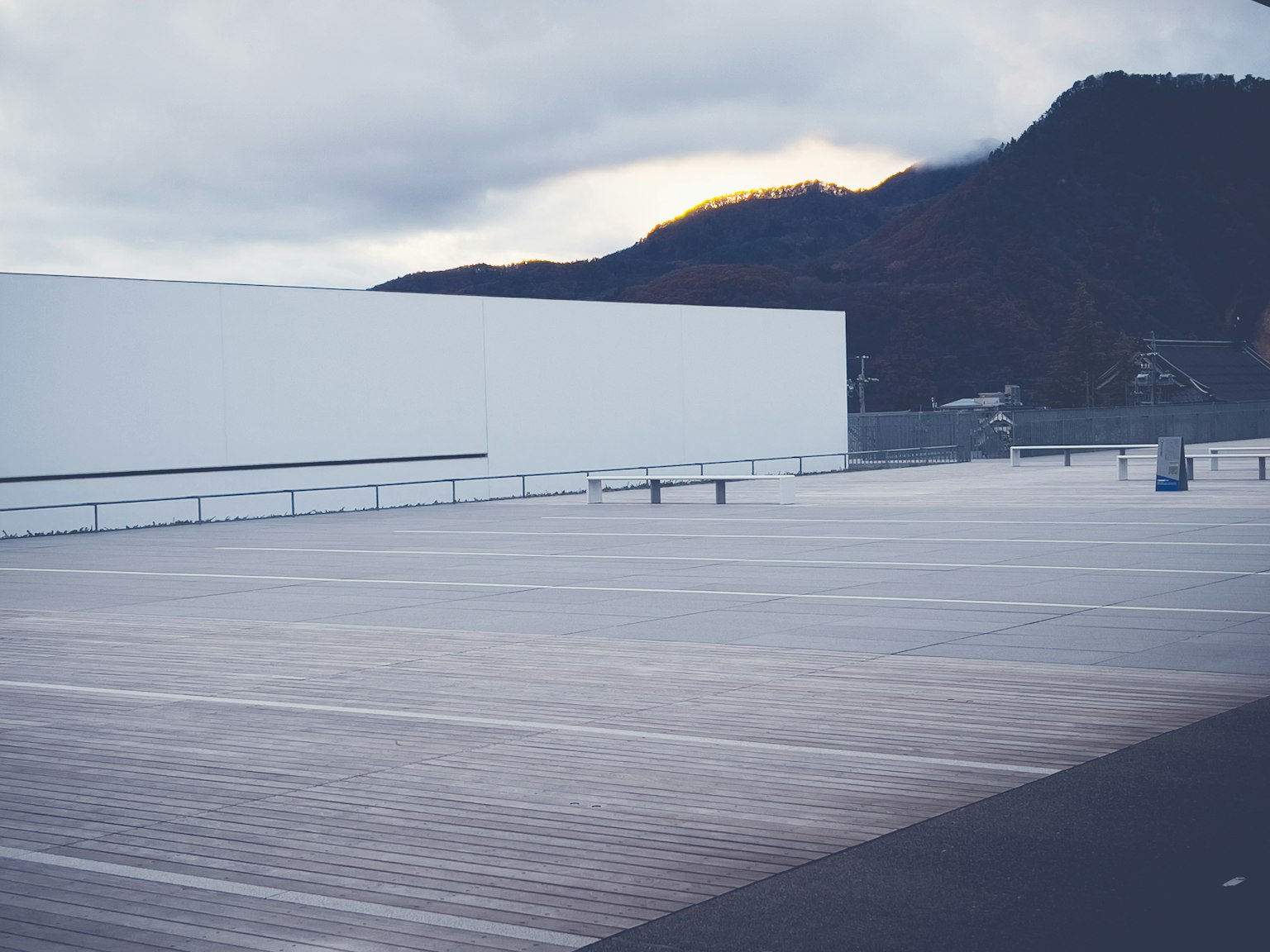 Vista de un edificio blanco con un amplio estacionamiento y fondo montañoso