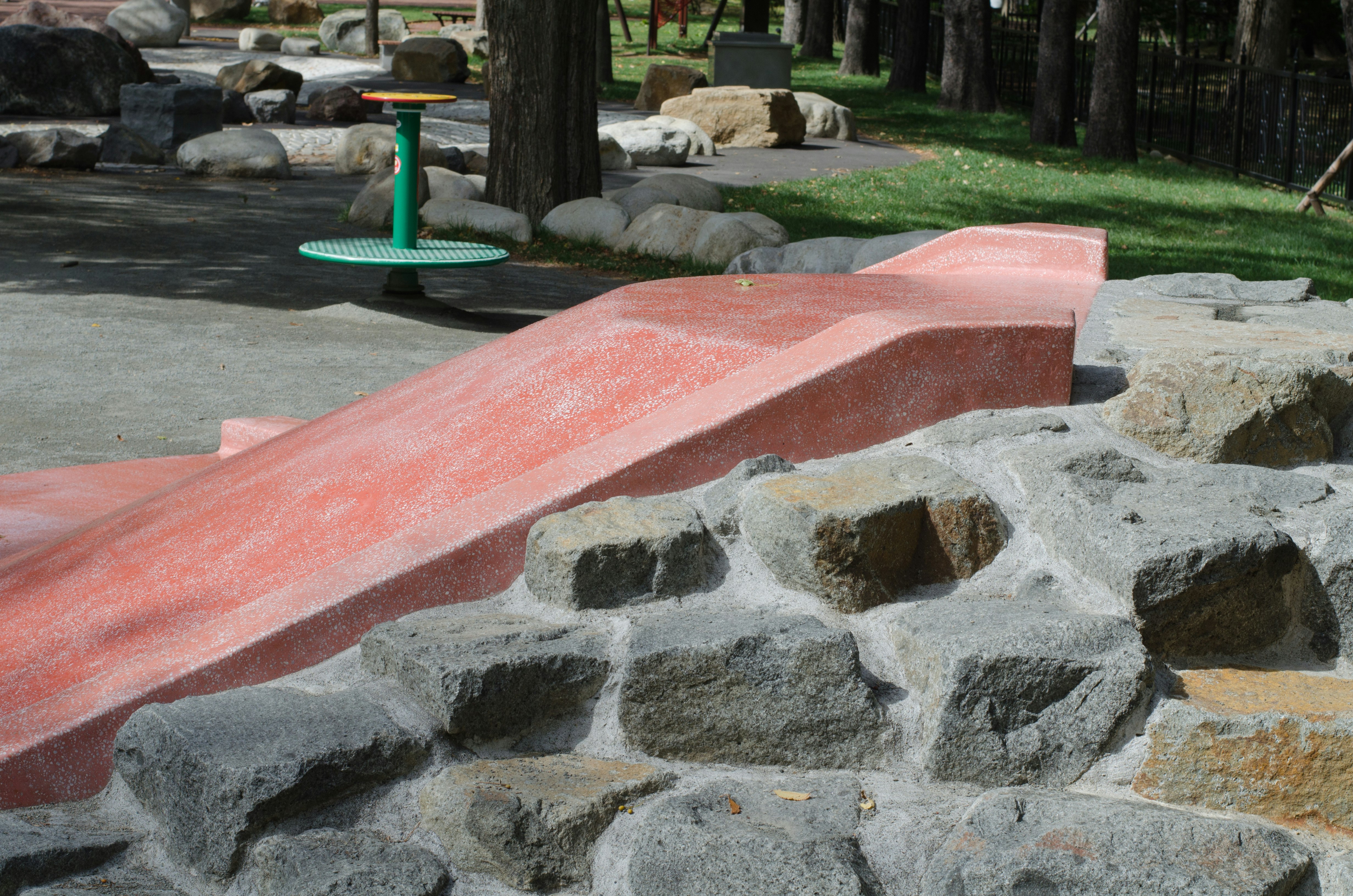 parque infantil con borde de piedras y tobogán rojo