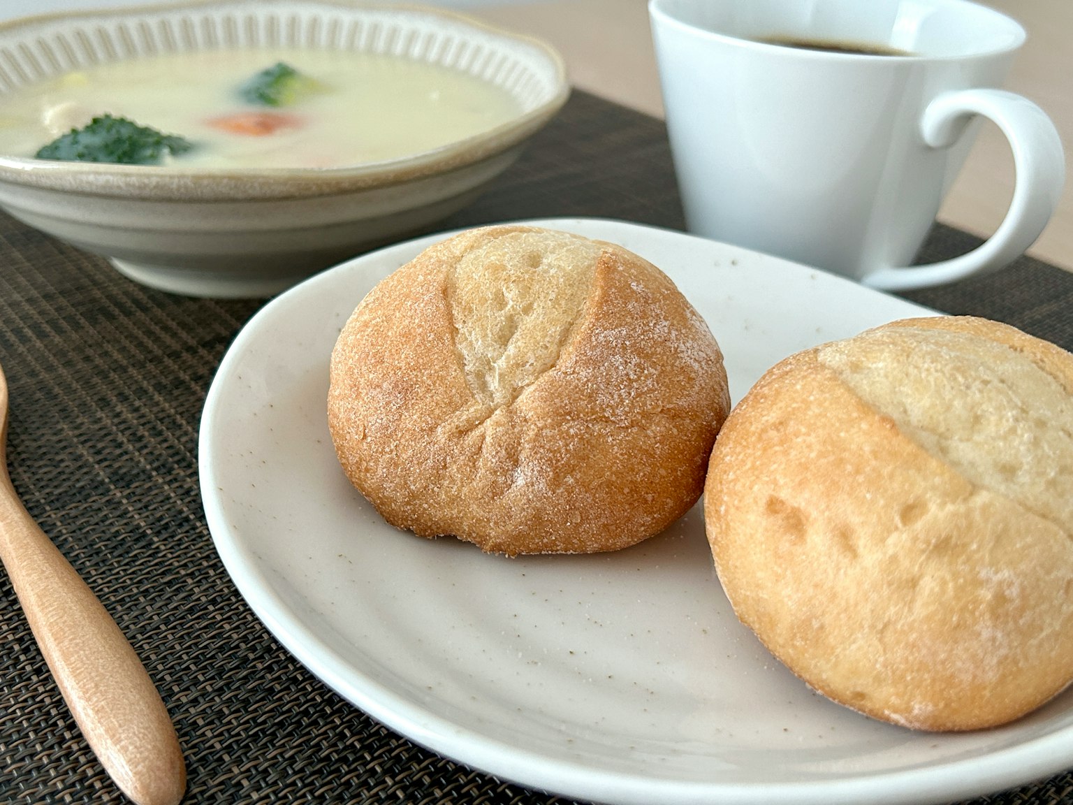Deux petits pains sur une assiette blanche avec un bol de soupe et une tasse de café