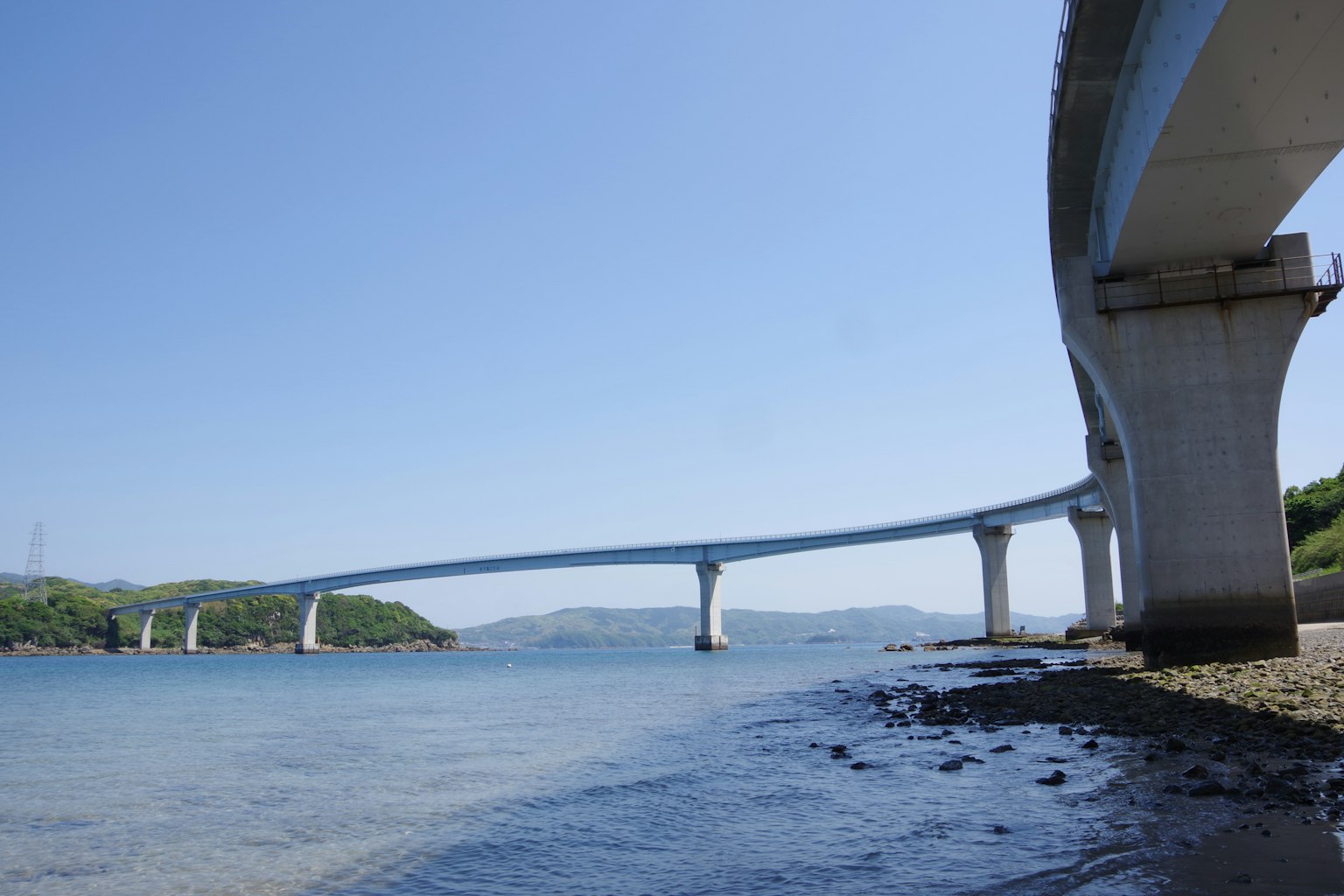 Blick auf eine Brücke über das Meer unter einem klaren blauen Himmel mit ruhigem Wasser und sichtbarem felsigem Ufer